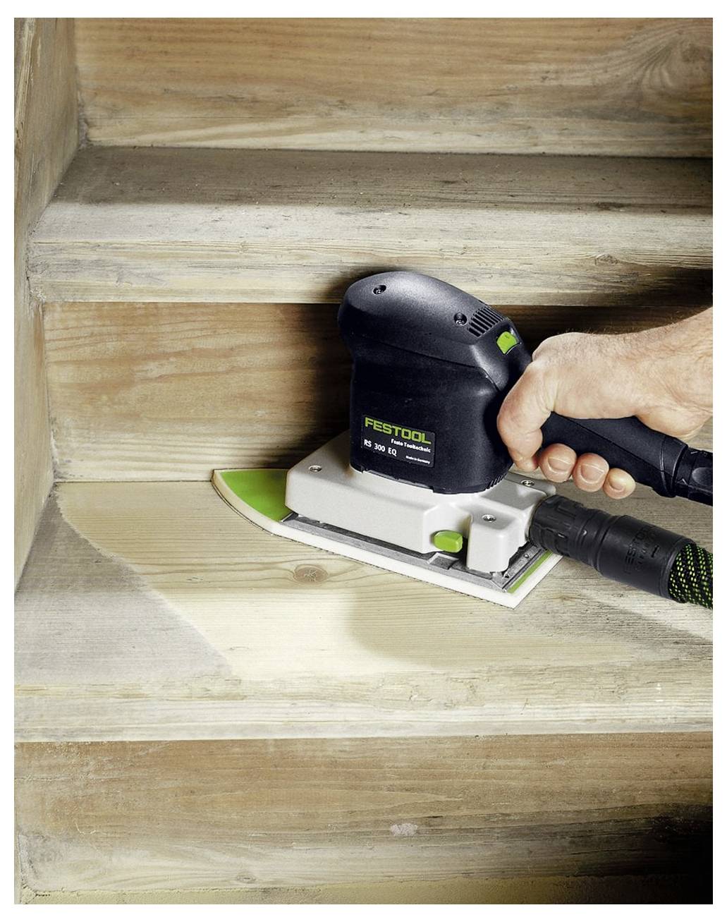 Una mano che utilizza una levigatrice elettrica per levigare e rifinire una scala in legno, rimuovendo lo strato superiore per rivelare il legno più pulito sottostante.