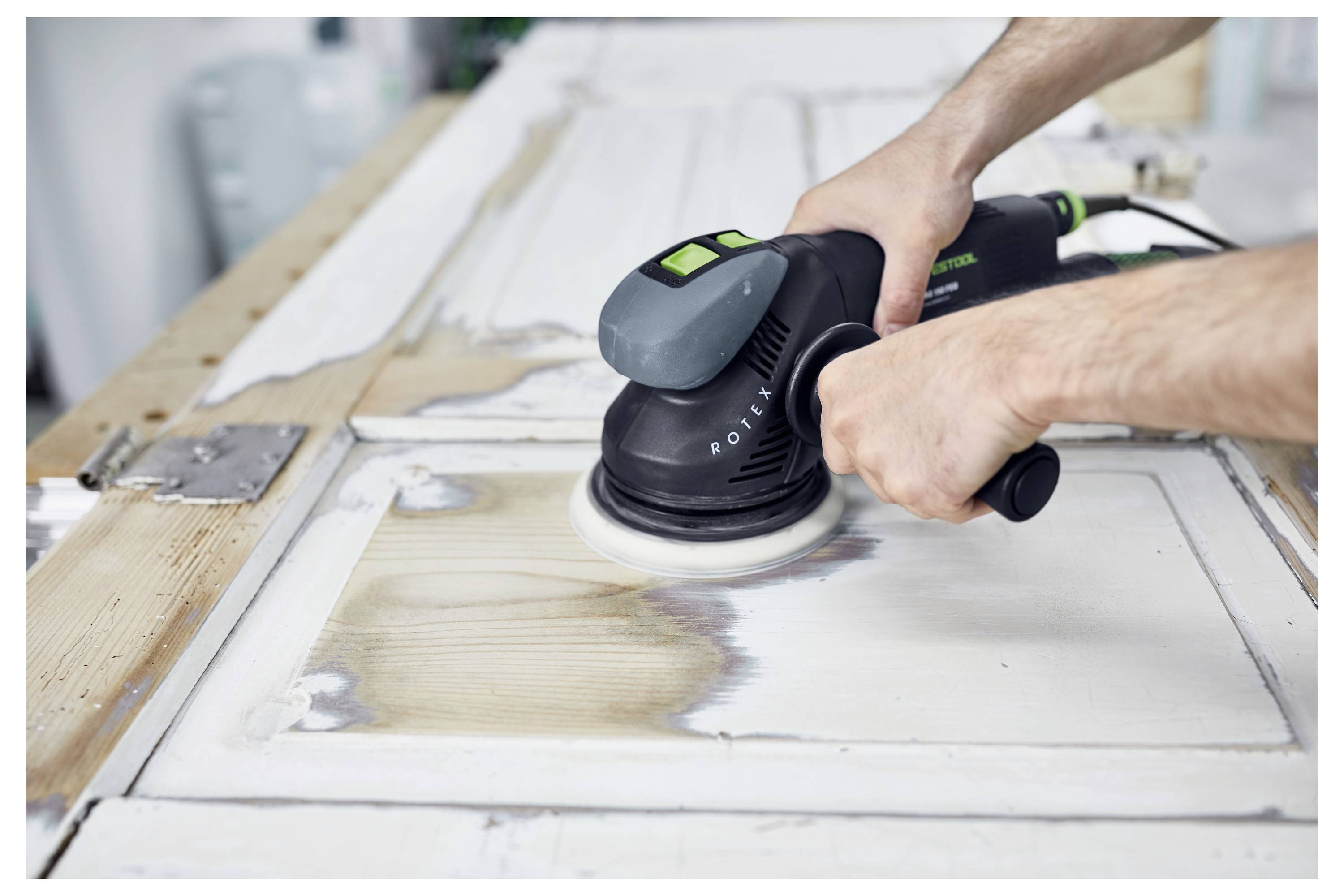 Una persona che indossa occhiali di sicurezza e una maschera utilizza una levigatrice elettrica su una parete, indicando un'attività di ristrutturazione domestica o costruzione.