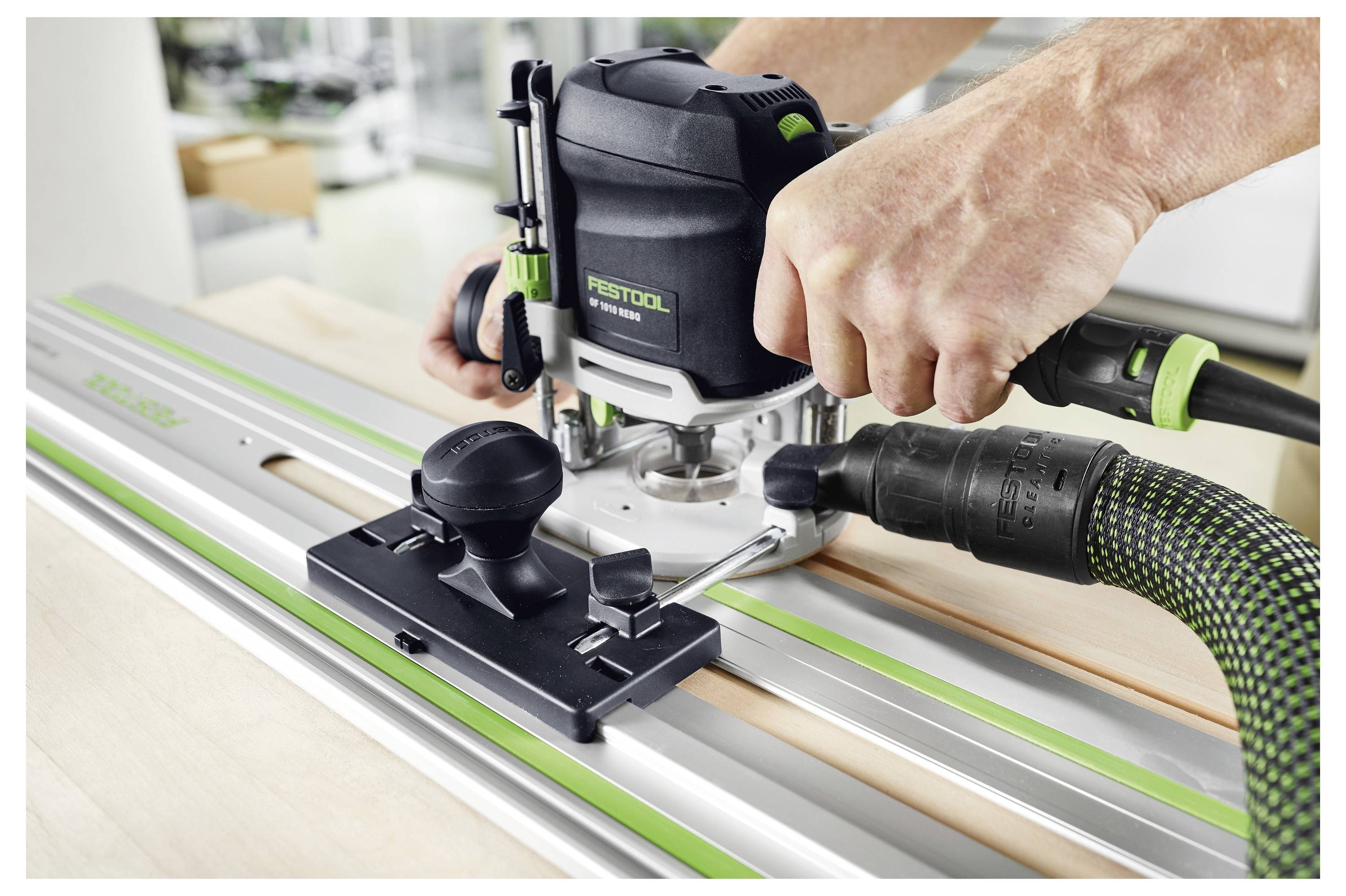 Una persona aziona un router Festool su una superficie di legno utilizzando una guida in alluminio. La configurazione mira a un taglio del legno preciso, evidenziando la sicurezza dello strumento e il controllo dell'operatore.