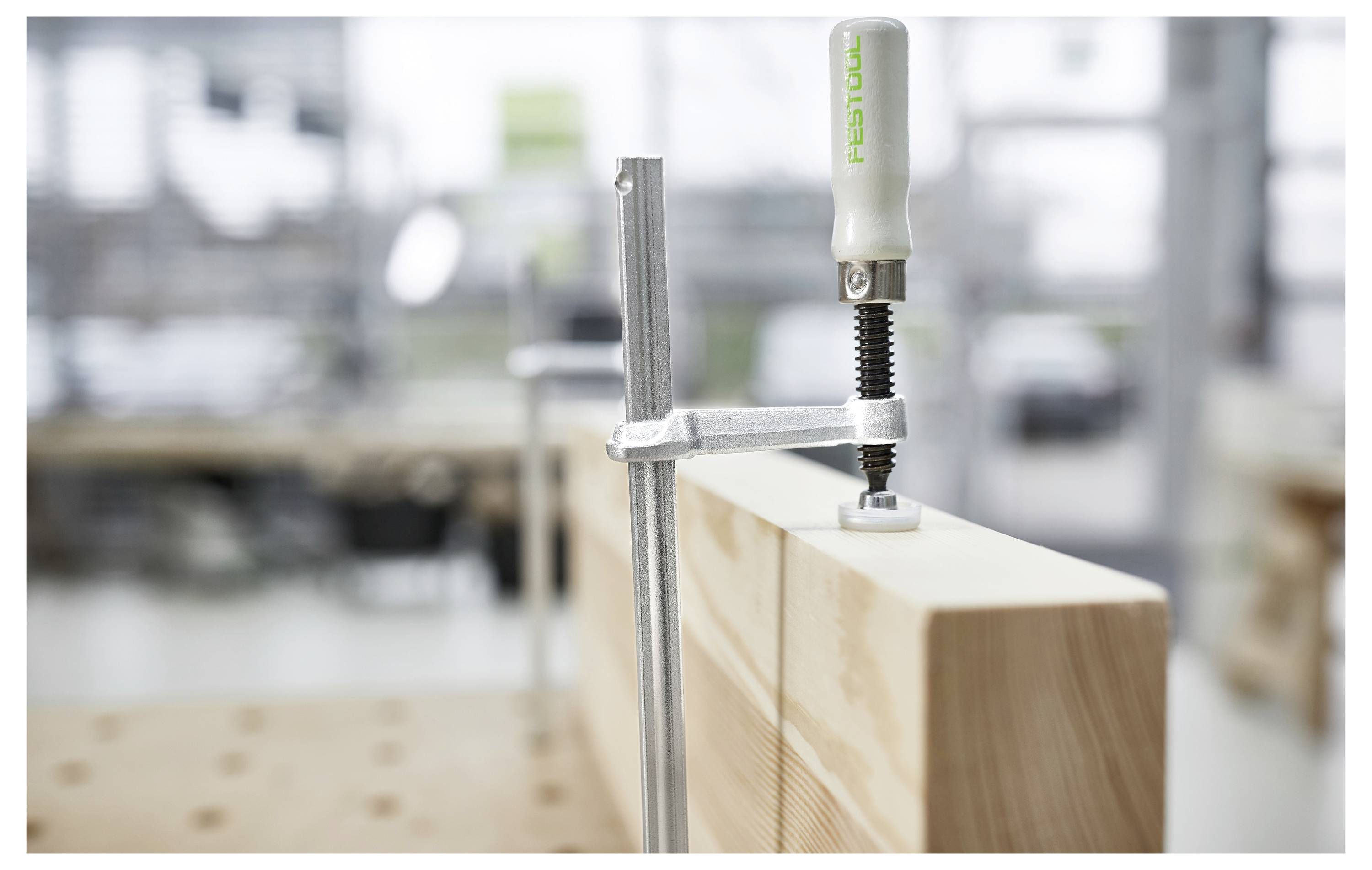 Una morsa in legno che tiene insieme pezzi di legno su un banco da lavoro in un laboratorio. Lo sfondo mostra attrezzi e attrezzature sfocati.