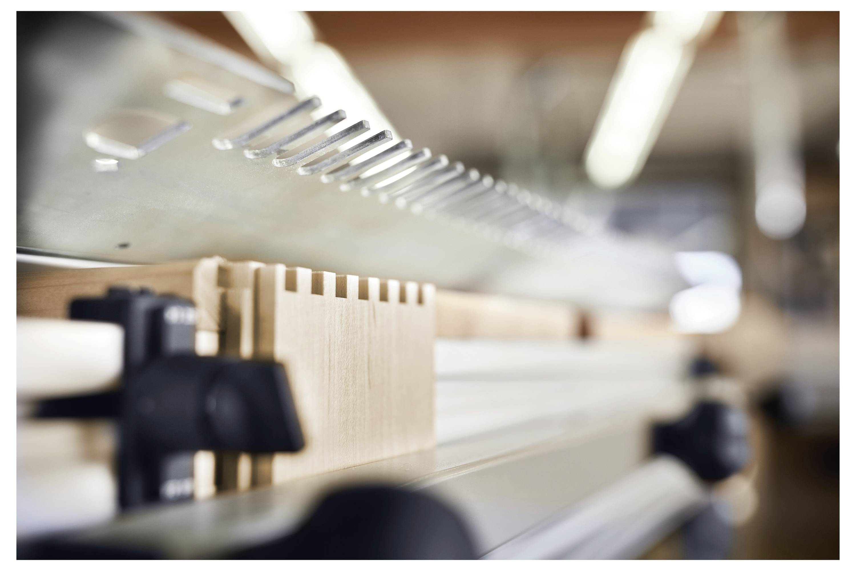 Primo piano di una configurazione di guida per code di rondine su un banco da lavoro, con focus sulla pettine metallica e il pezzo in legno, sfondo di officina sfocato.