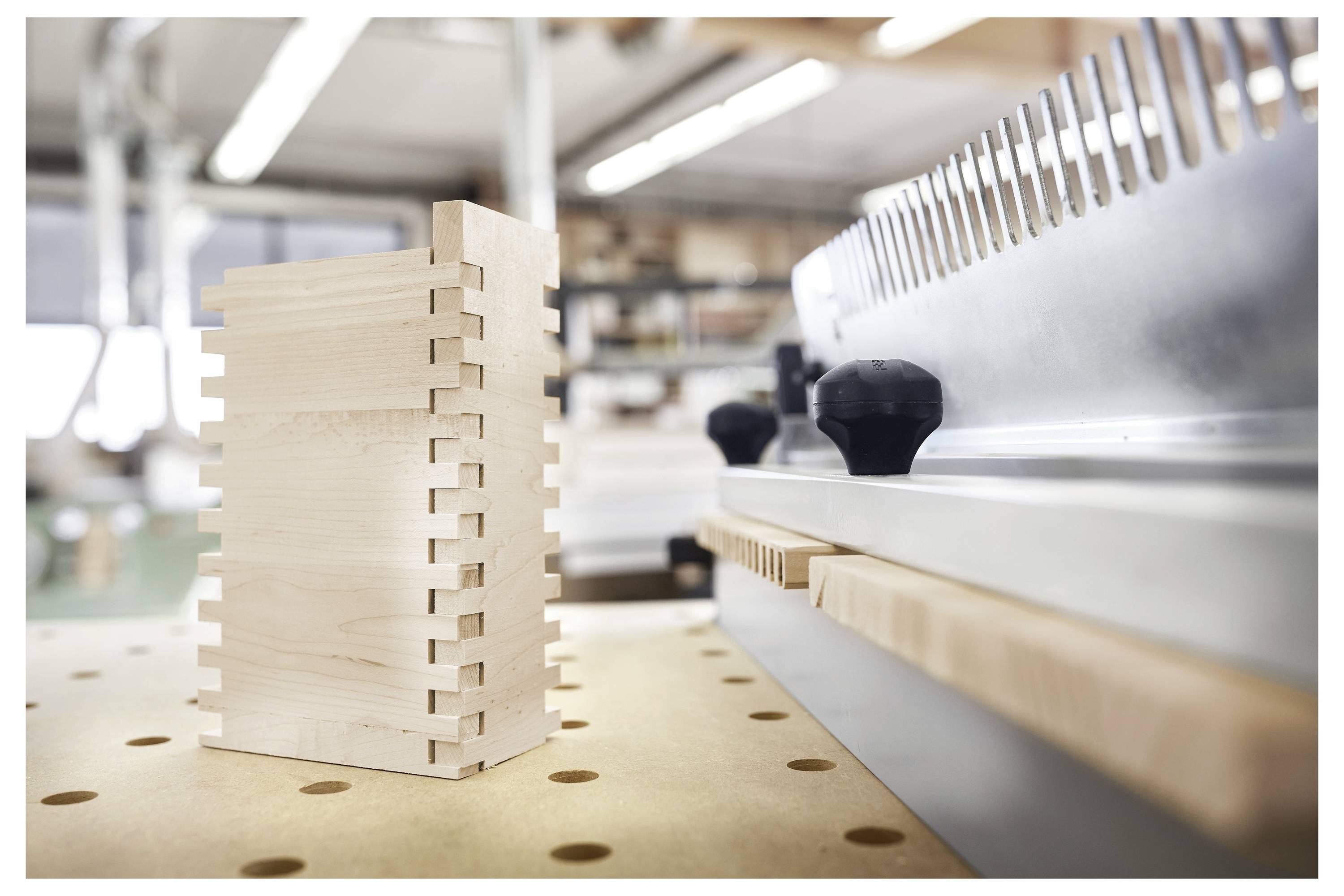 'Un primo piano di una macchina per la lavorazione del legno con focus su un pezzo di legno in fase di sagomatura con precisione da guide metalliche in un ambiente di laboratorio artigianale.'