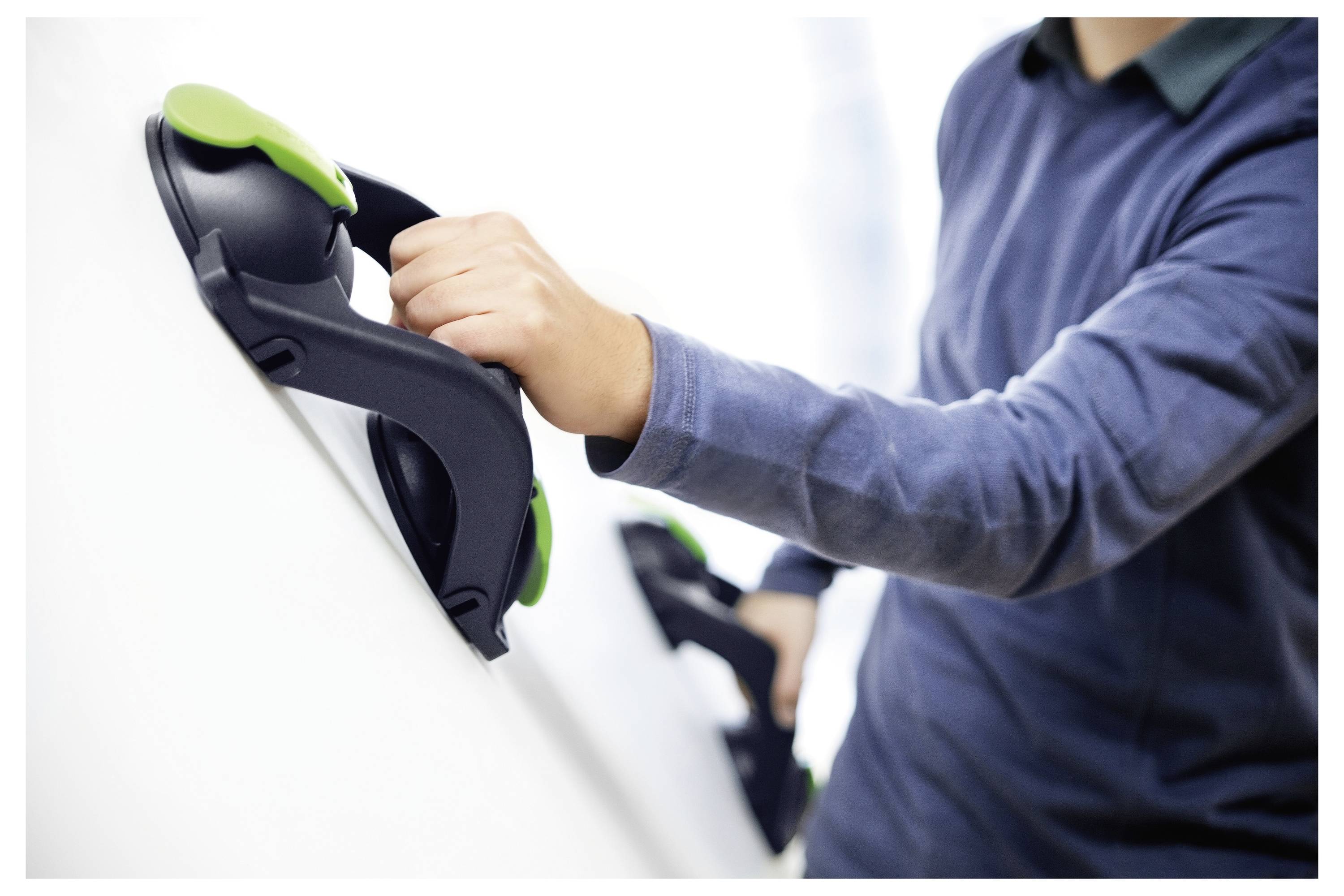 Una persona che utilizza ventose ergonomiche per sollevare una grande superficie liscia, suggerendo un'attività che comporta lo spostamento o l'installazione di pesanti pannelli.