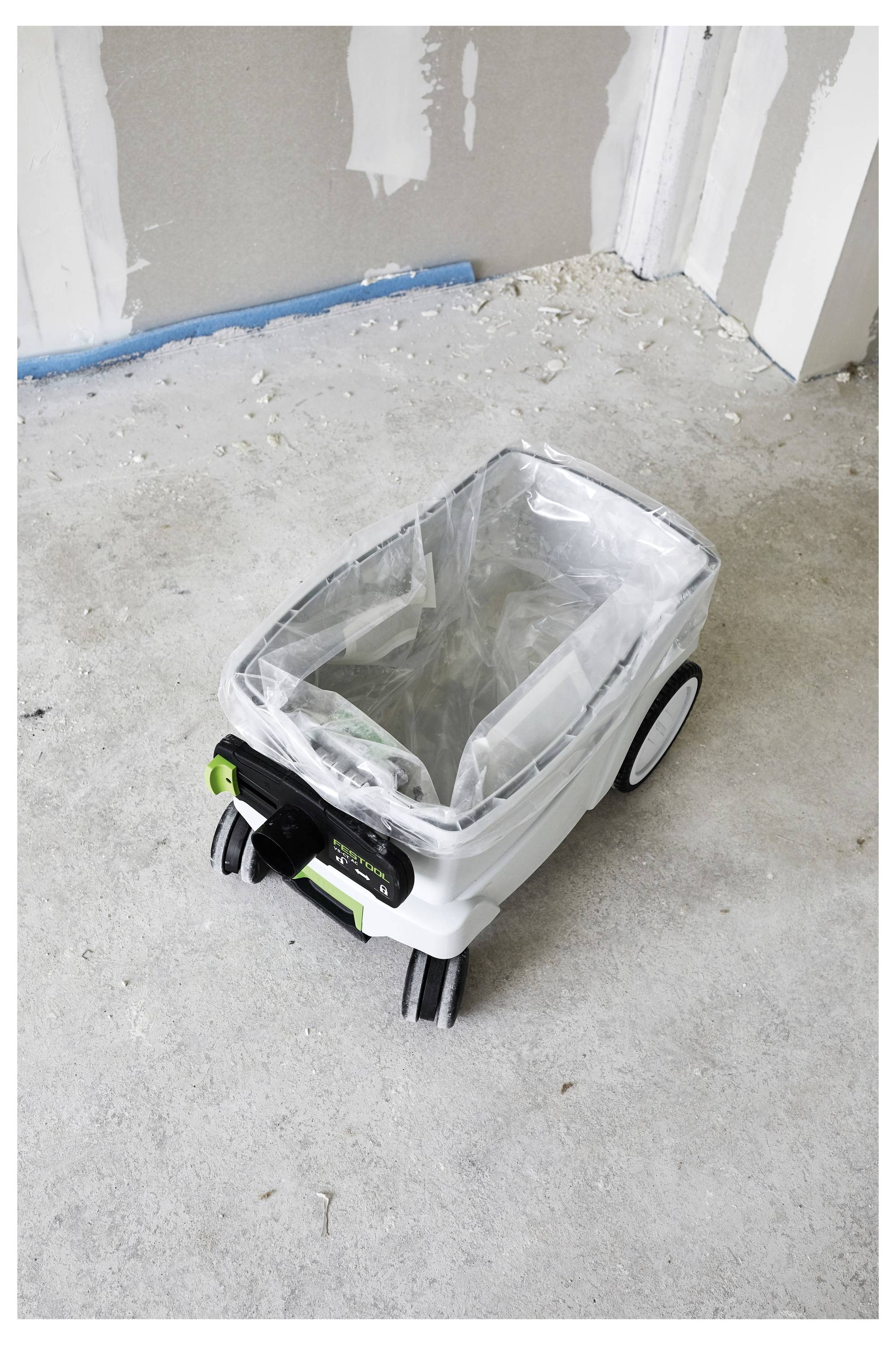 Un piccolo contenitore di stoccaggio con ruote e rivestimento in plastica, posizionato su un pavimento non finito in una stanza con pareti parzialmente dipinte.