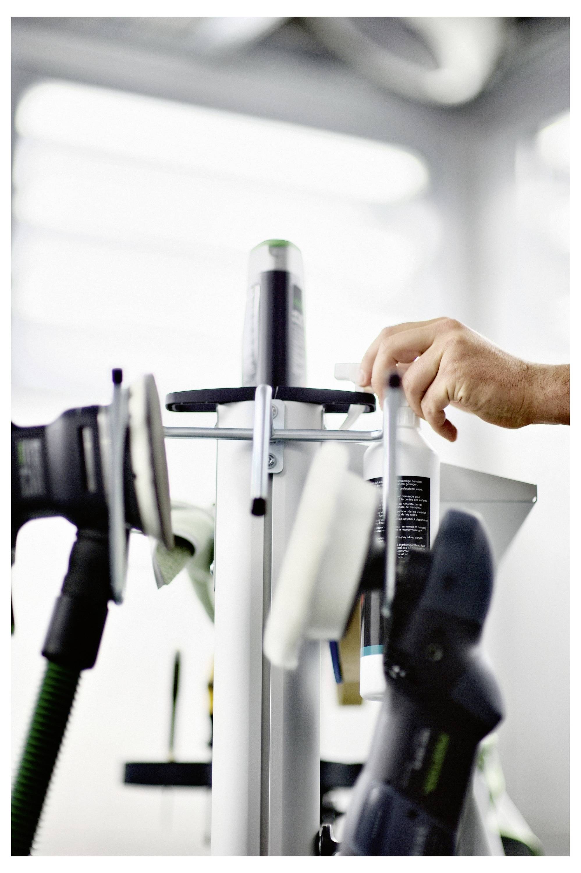 La mano di una persona regola gli attrezzi su un supporto in un laboratorio, suggerendo la preparazione per un compito o un progetto. Gli attrezzi includono levigatrici e un rullo.