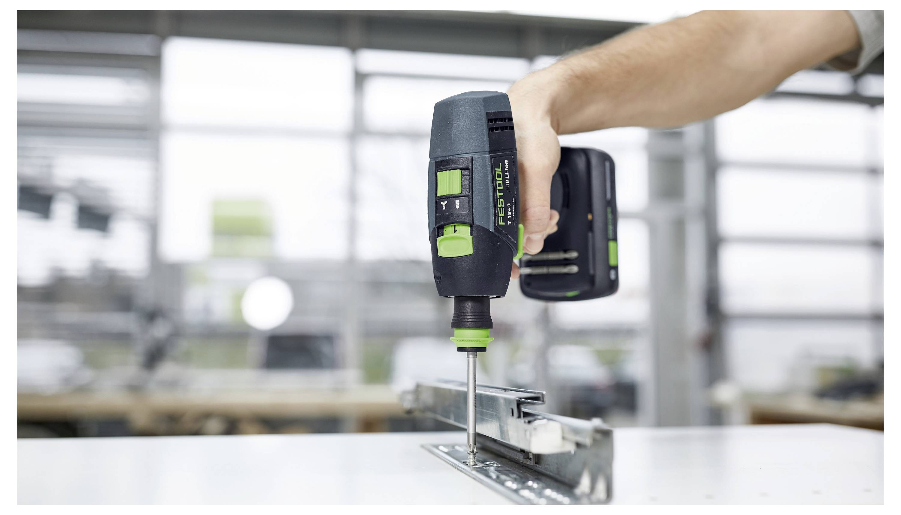 La mano di una persona che utilizza un trapano senza fili per assemblare una guida di mobili su un banco da lavoro in un ambiente di laboratorio.