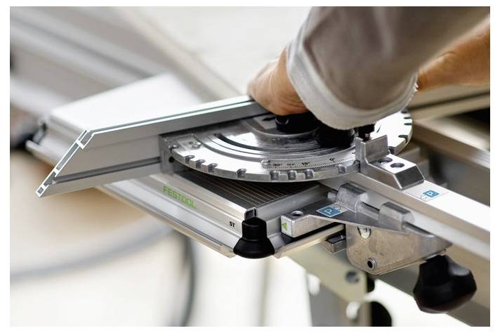 Una persona regola un calibro a squadra circolare per tagli precisi su una sega. Il calibro è metallico con angoli marcati per l'accuratezza.