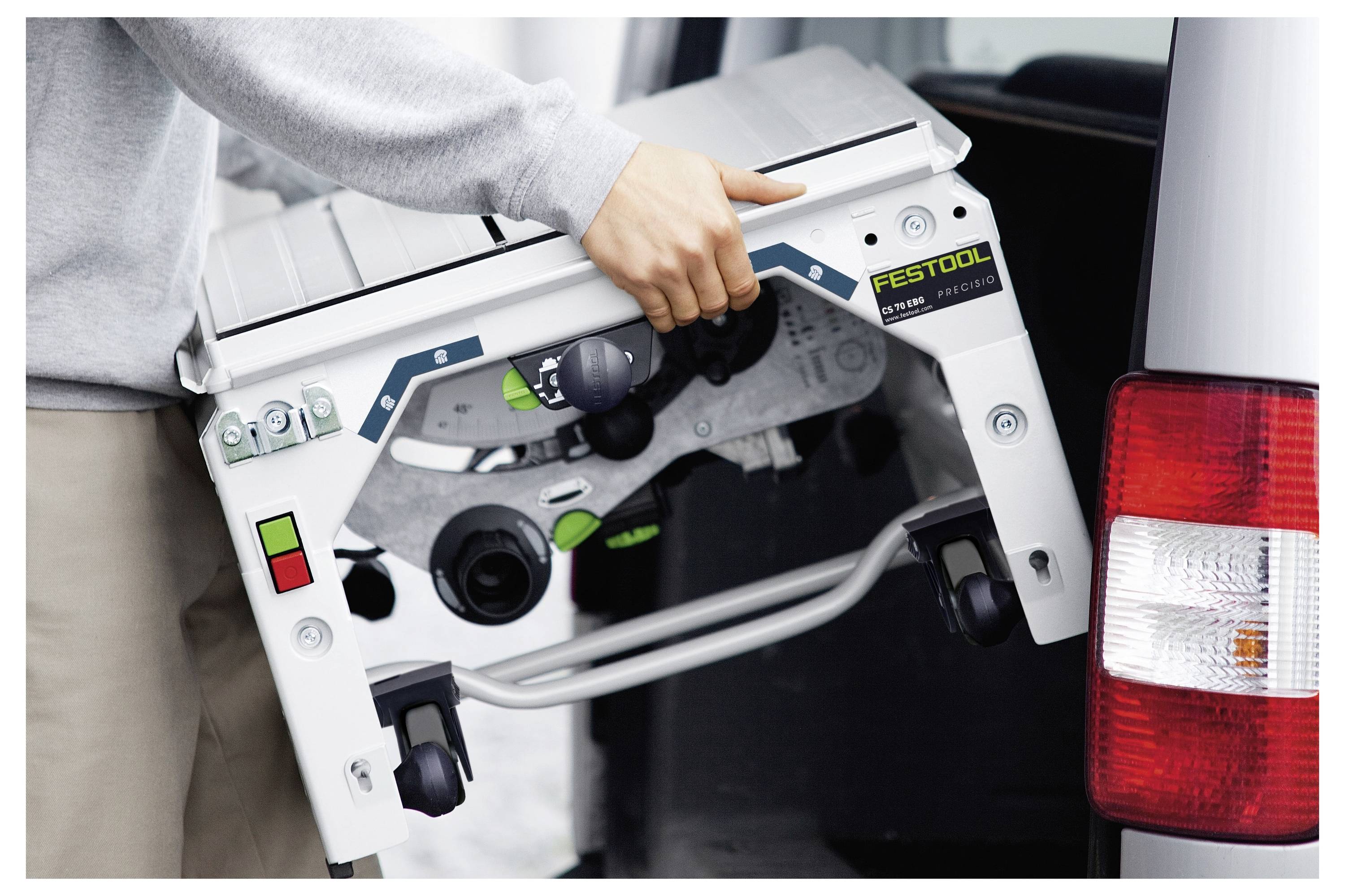 Una persona carica un'elettrosega da banco compatta Festool in un veicolo, evidenziando la portabilità dello strumento e la facilità di trasporto.