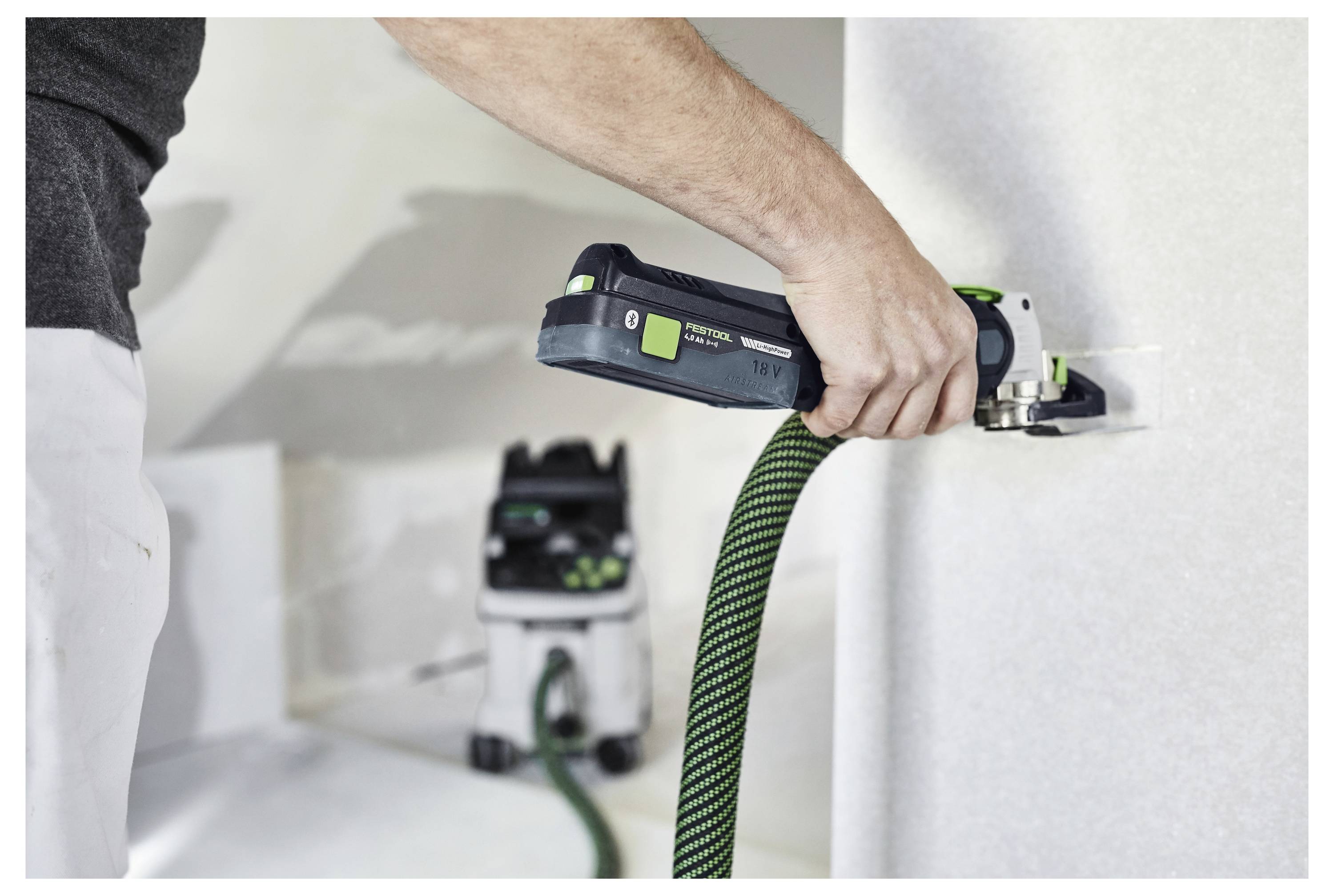 Una persona utilizza un utensile elettrico collegato a un sistema di aspirazione per l'estrazione della polvere mentre lavora su una parete.