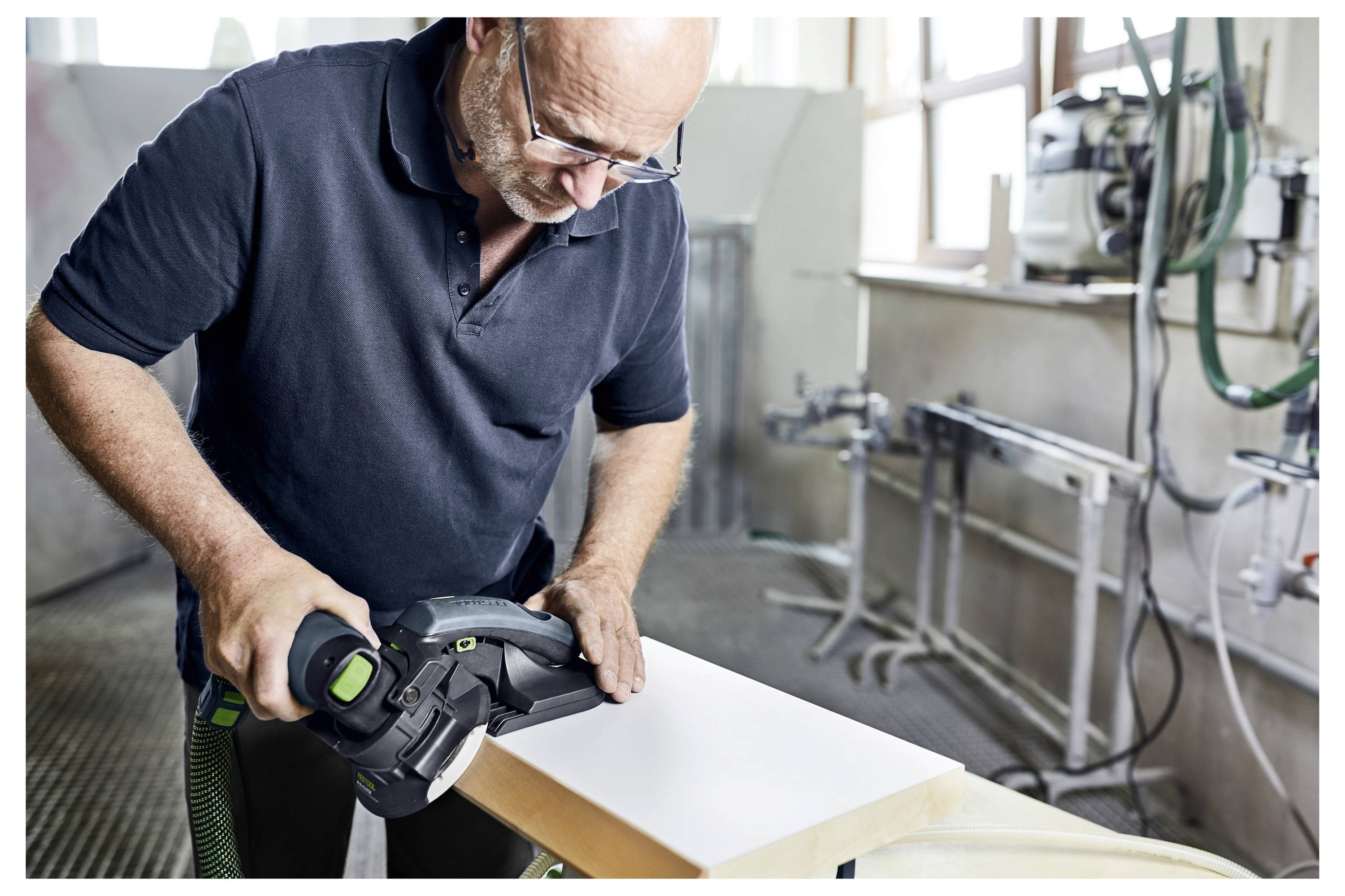 Una persona in un laboratorio utilizza una levigatrice elettrica su una tavola di legno, levigando la sua superficie. Attrezzi e macchinari da laboratorio sono visibili sullo sfondo.