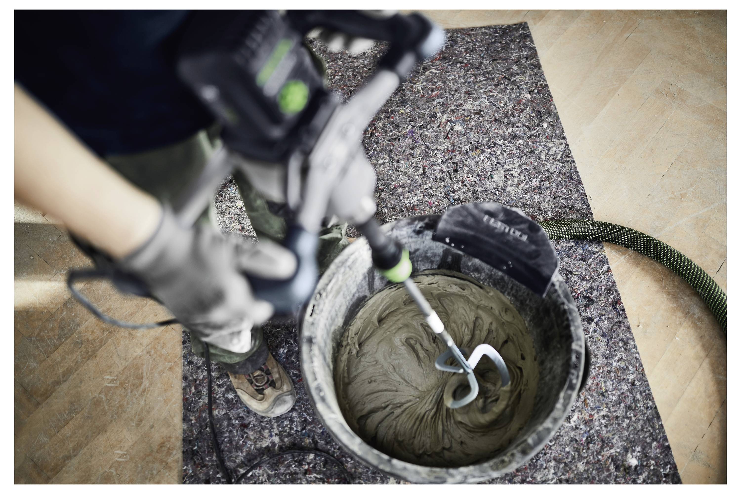 Una persona utilizza un trapano elettrico con un accessorio per mescolare per agitare il materiale in un secchio, probabilmente preparando materiale da costruzione per un'attività di costruzione.