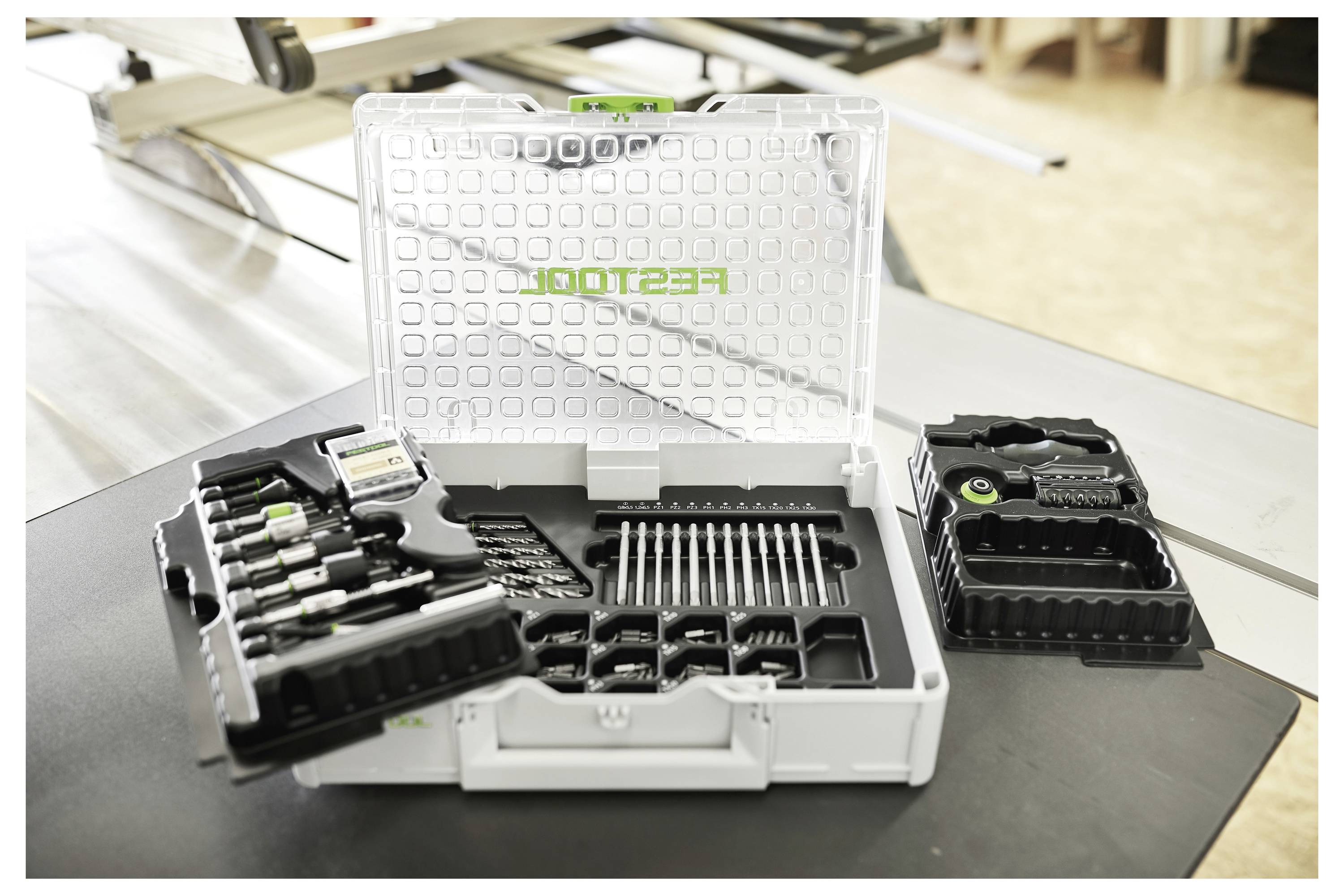 Una persona attacca un tubo flessibile a un aspiratore di polvere Festool bianco su un tappeto blu, dimostrando la configurazione dell'attrezzatura.