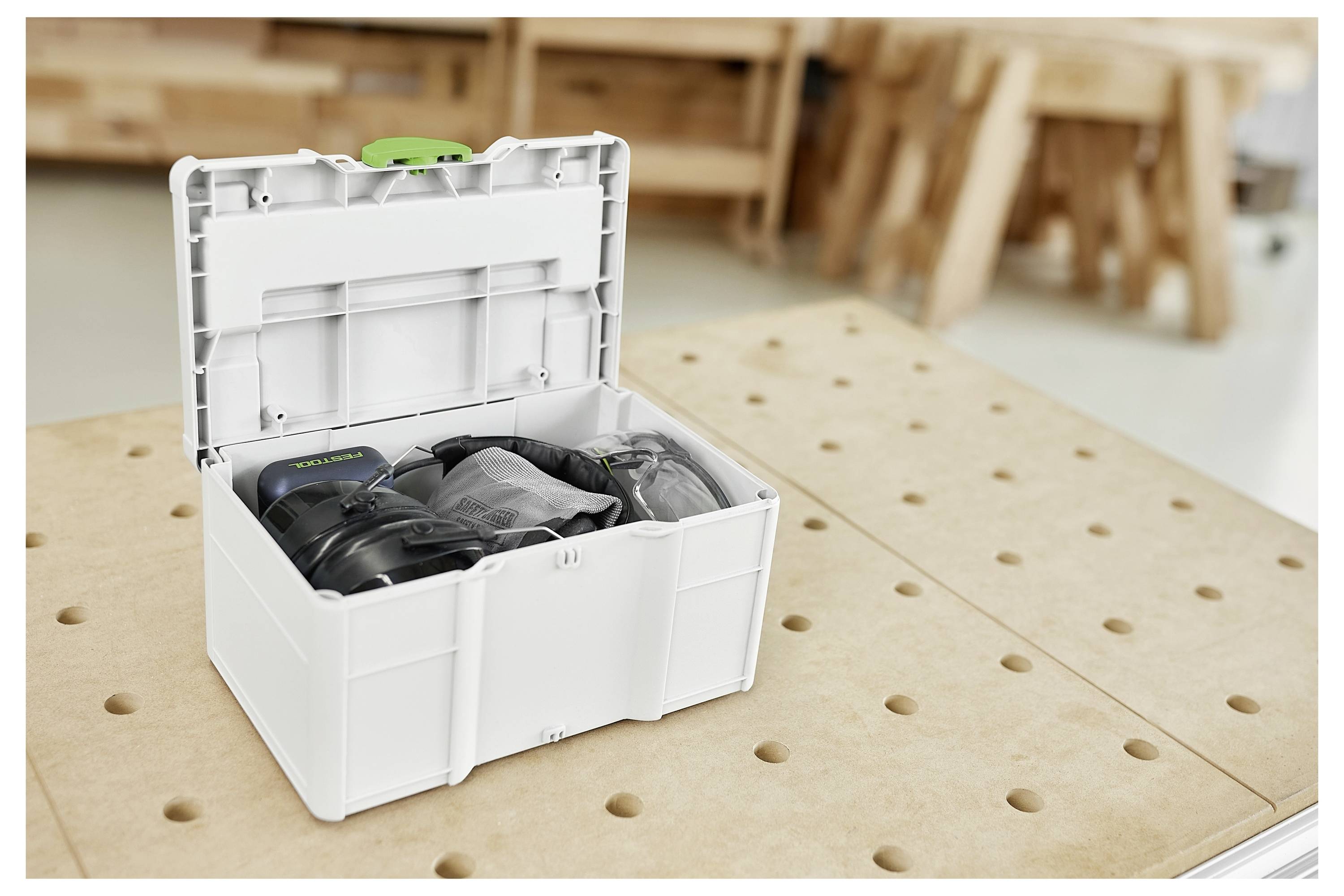 Una scatola di stoccaggio bianca aperta su un banco da lavoro perforato contiene vari attrezzi e accessori in un ambiente di officina.