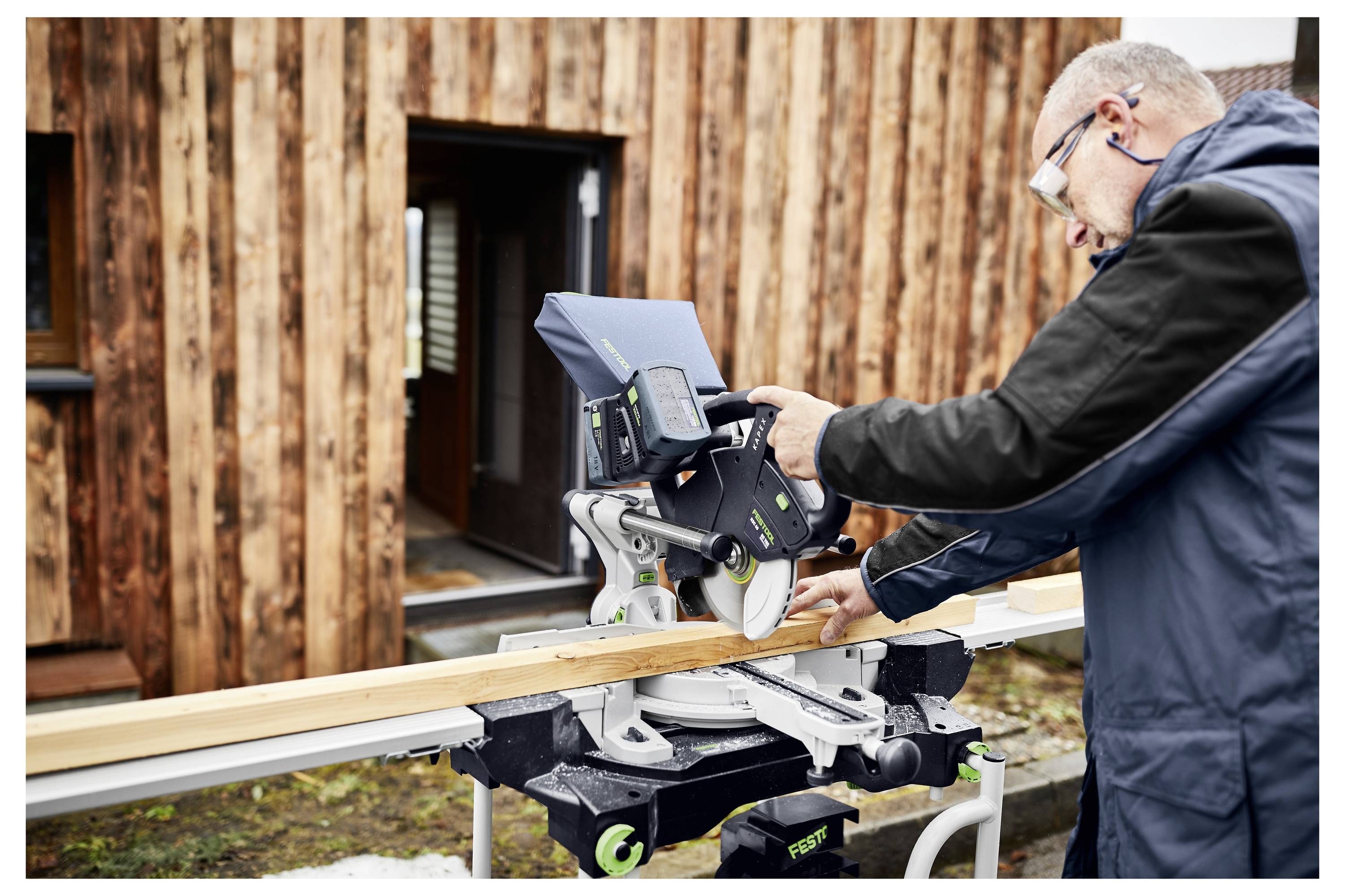 Una persona che trasporta un estrattore di polvere Festool su una scala in legno, indicando la portabilità e la facilità d'uso per i compiti di pulizia.