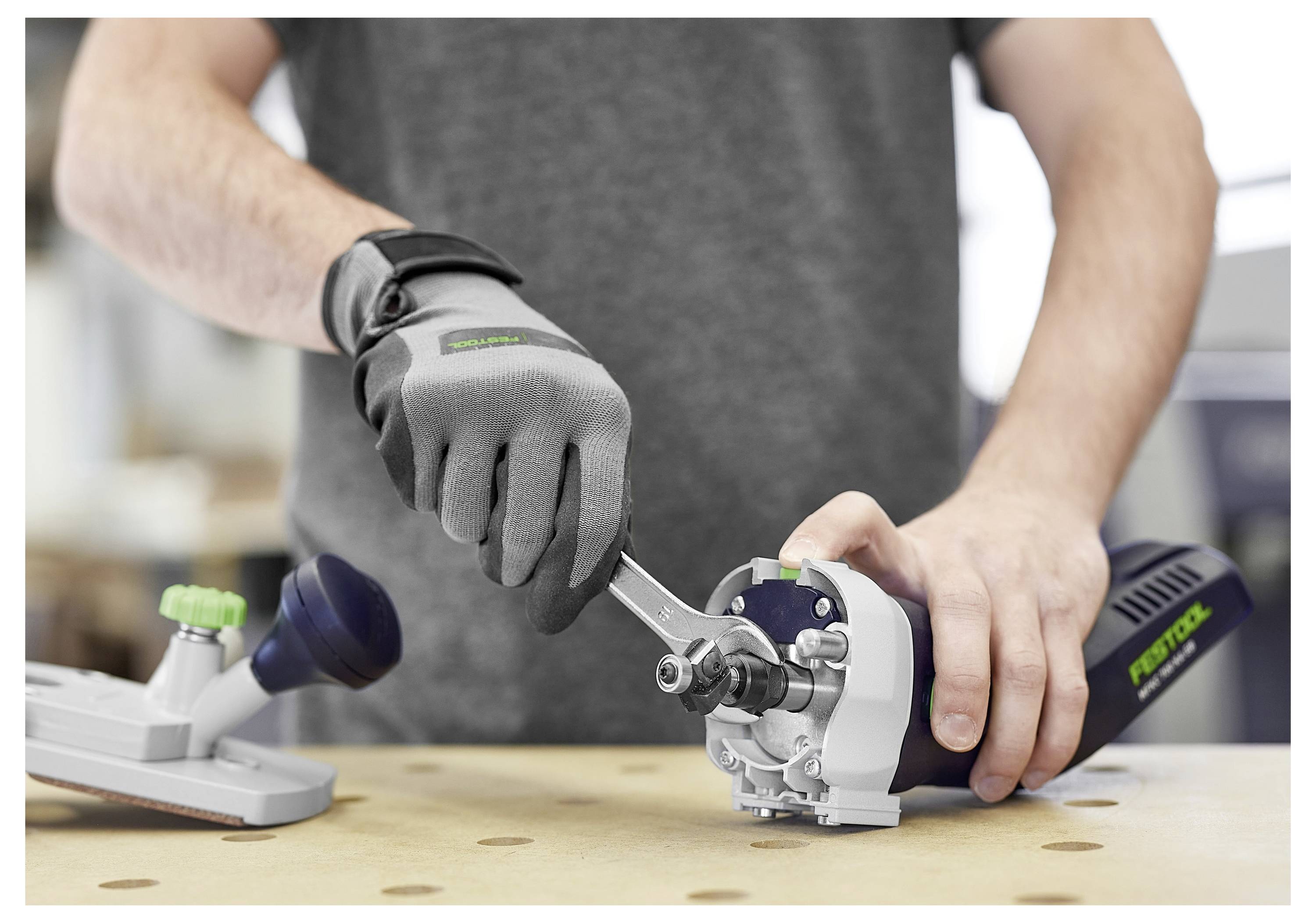 Una persona che indossa guanti grigi regola uno strumento usando una chiave, concentrandosi sul meccanismo dell'attrezzatura, su un tavolo da laboratorio.