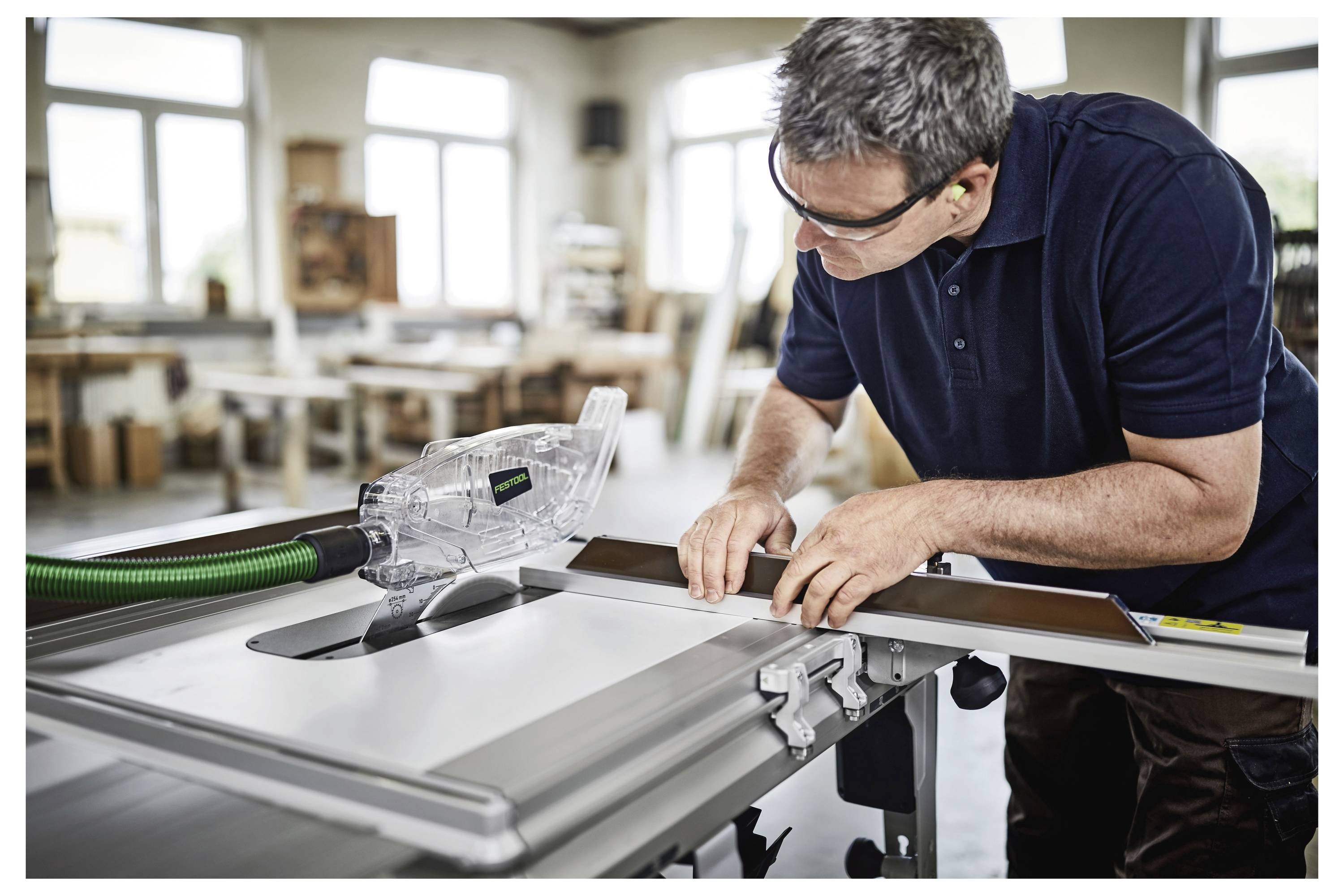 Una persona che indossa occhiali di protezione utilizza una sega circolare da banco per tagliare il legno in un laboratorio ben illuminato.