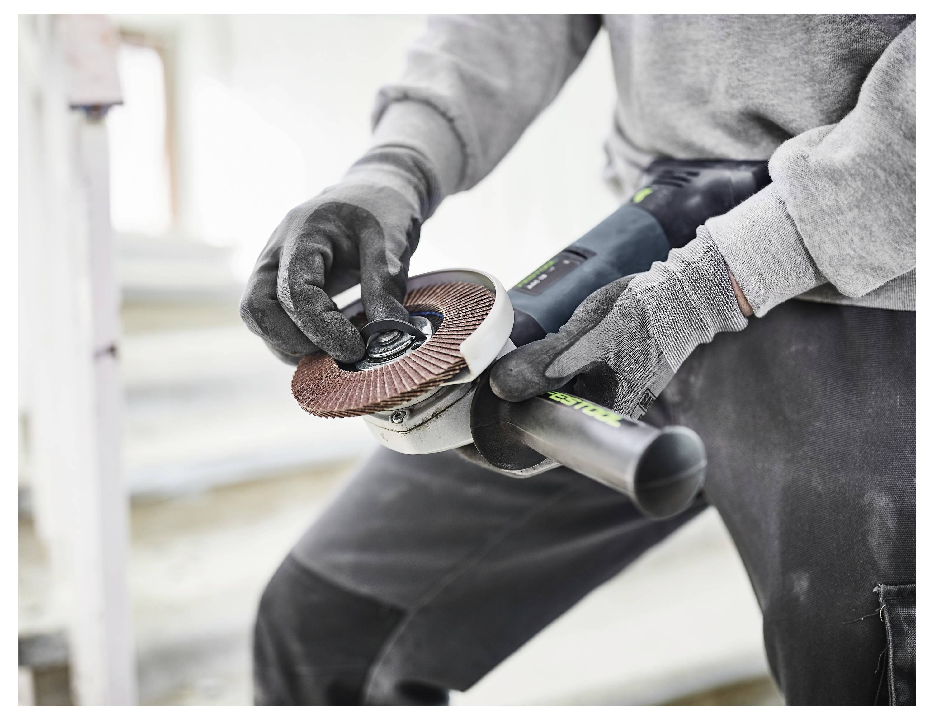 Una persona che indossa guanti utilizza una smerigliatrice angolare in un cantiere, concentrandosi sulla regolazione dello strumento.