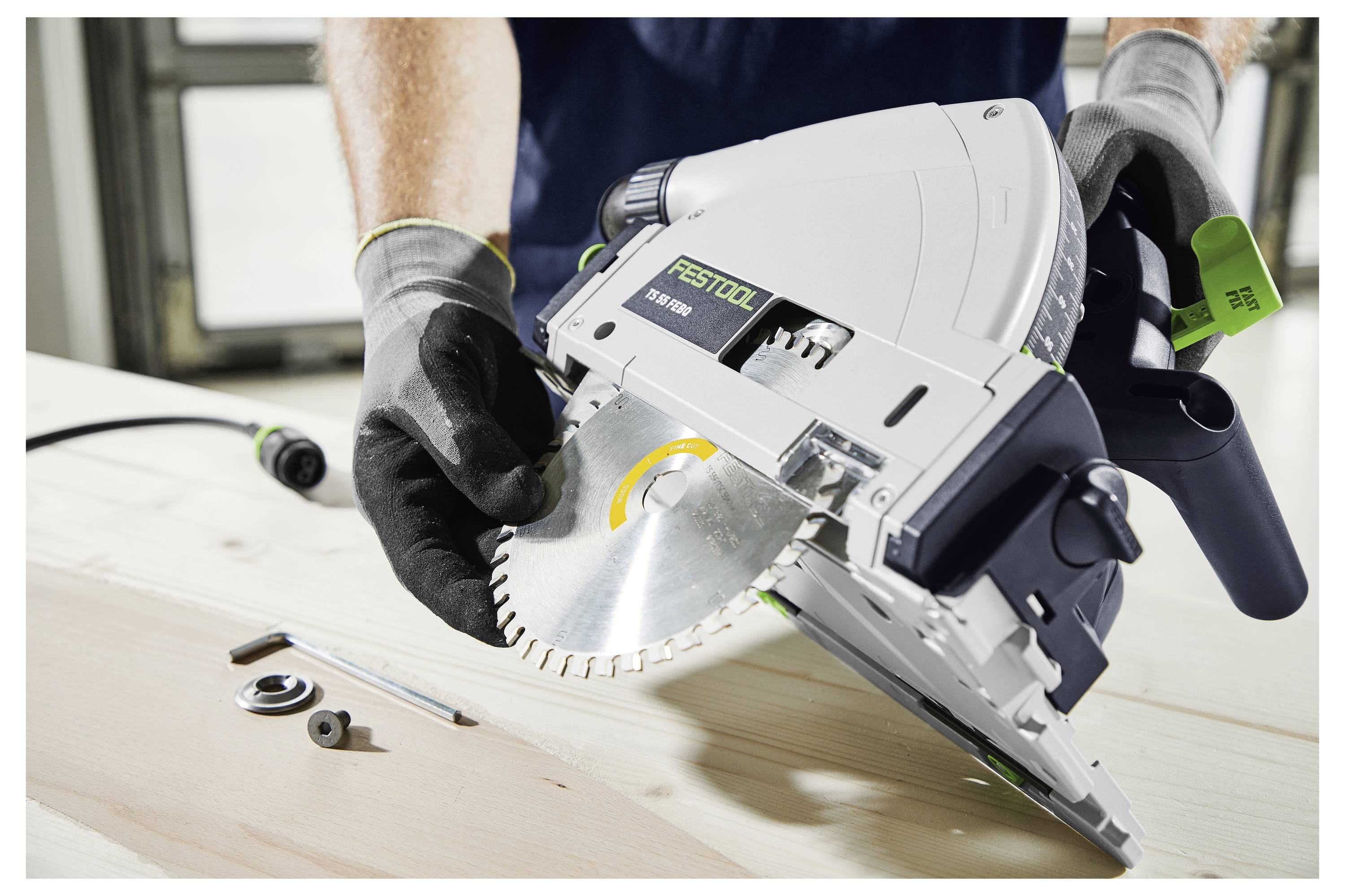 Una persona che indossa guanti sta regolando una lama di sega circolare su uno strumento Festool, con varie parti e la sega su una superficie di legno.