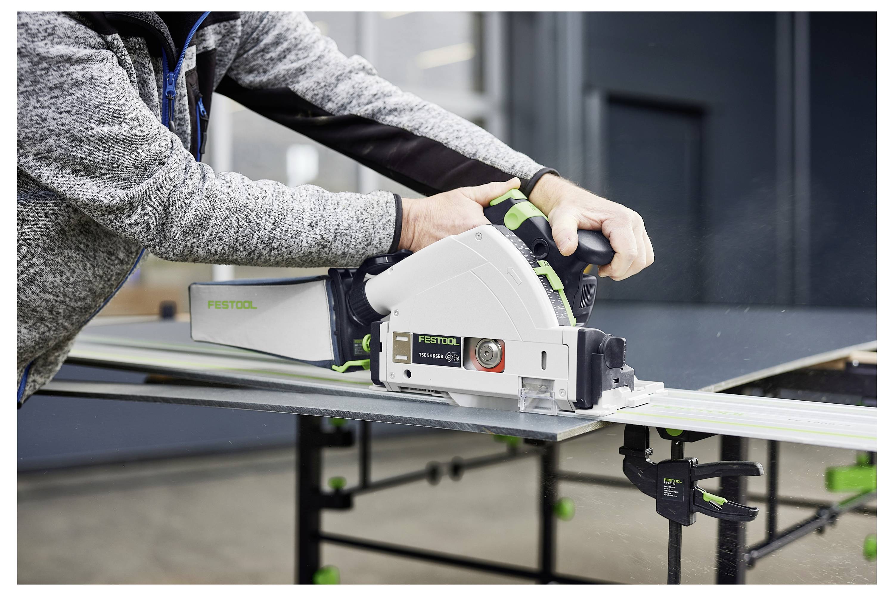 Una persona che utilizza una sega da traccia Festool per tagliare un foglio di materiale su un banco da lavoro, mostrando attrezzi per la lavorazione del legno o l'edilizia in uso.
