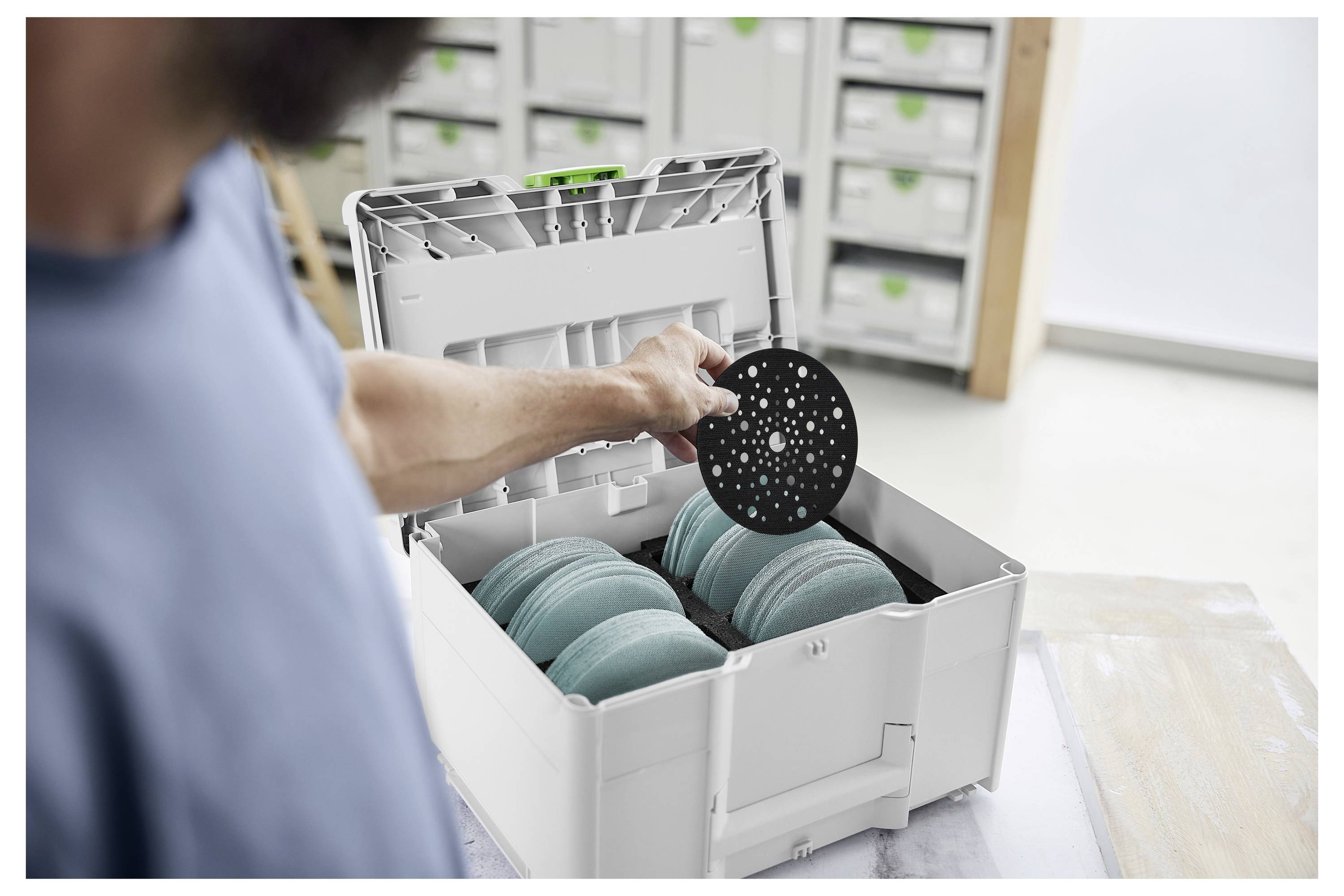 Una persona mette un disco circolare nero in una scatola di stoccaggio aperta piena di dischi color teal, in un ambiente di laboratorio ben organizzato.