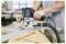 Una persona utilizza uno strumento router per incidere scanalature precise in una tavola di legno su un banco da lavoro. Lo strumento è etichettato 'Festool'.