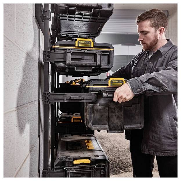 Una persona organizza robusti scatoloni per attrezzi neri e gialli su uno scaffale montato a parete in un garage, enfatizzando uno stoccaggio efficiente.