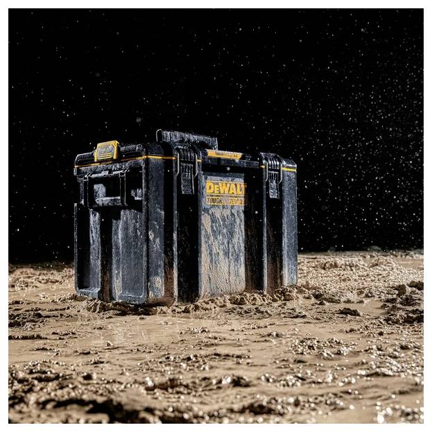 Una cassetta degli attrezzi nera e gialla coperta di fango si trova su un terreno bagnato e fangoso con spruzzi d'acqua intorno, che mette in evidenza il suo design robusto e impermeabile.