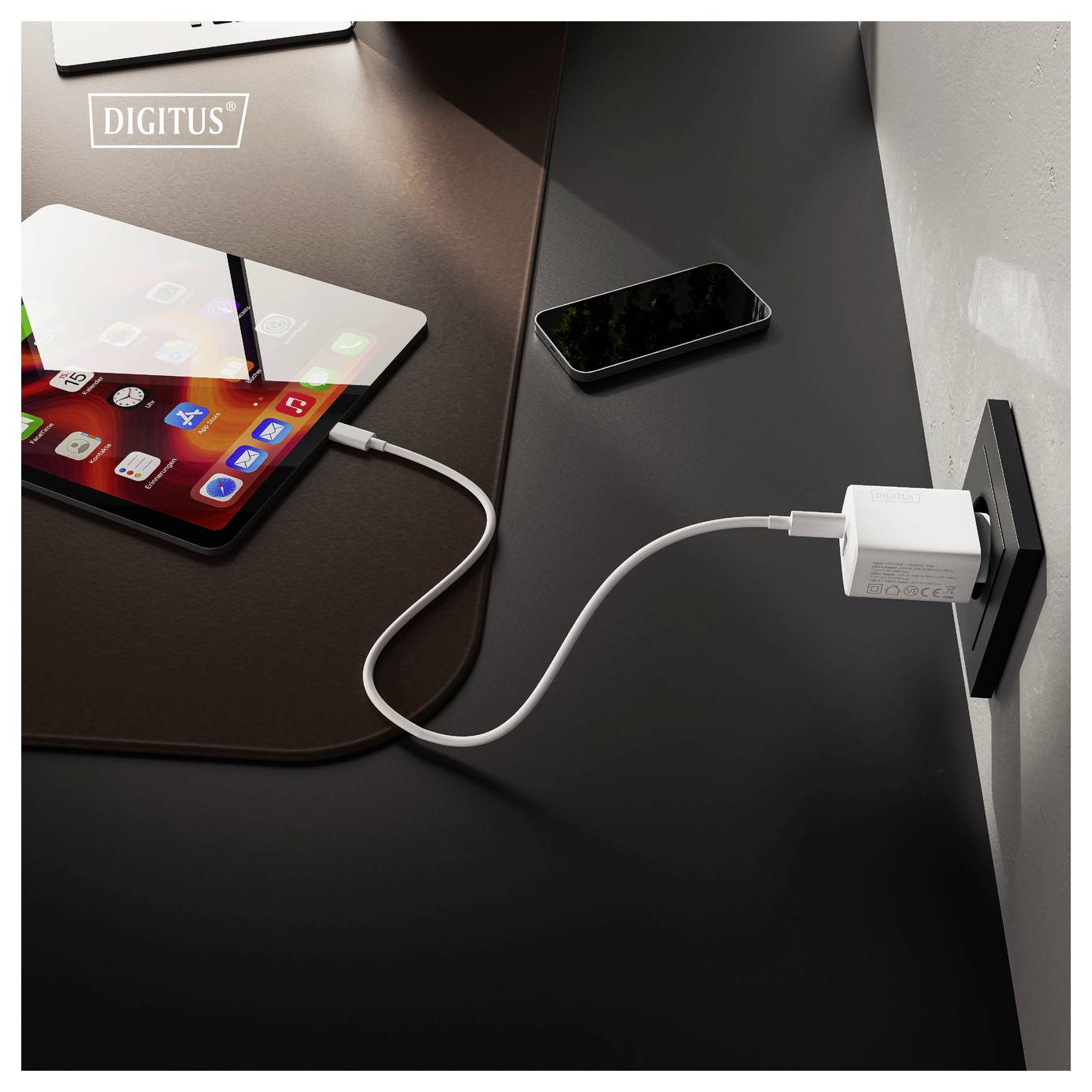 Un tablet e uno smartphone su una scrivania, con il tablet collegato a un caricabatterie da muro tramite un cavo USB.
