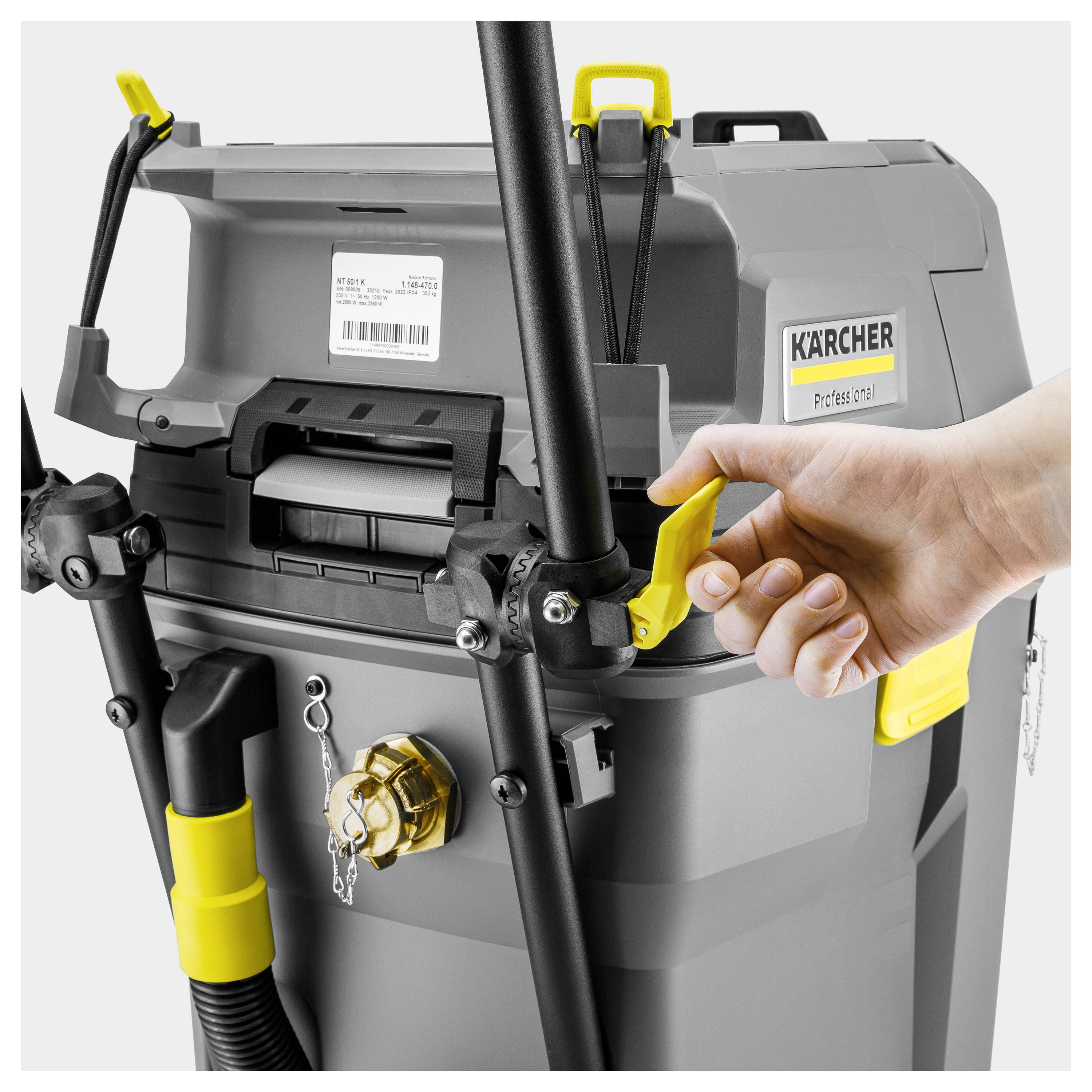 Una persona sta aprendo un aspirapolvere industriale grigio di Kärcher utilizzando un chiavistello giallo, circondato da accessori neri e gialli.