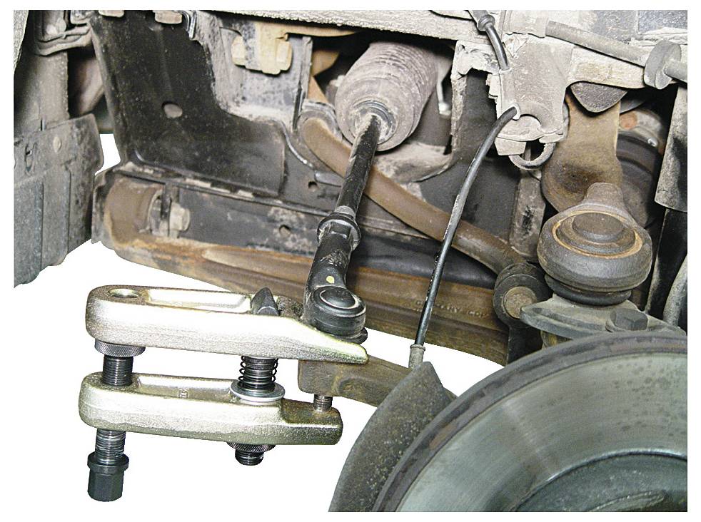 L'immagine mostra uno strumento separatore di snodi sferici in uso, che rimuove uno snodo sferico da un assieme di sospensione di un'auto, evidenziando la riparazione automobilistica.