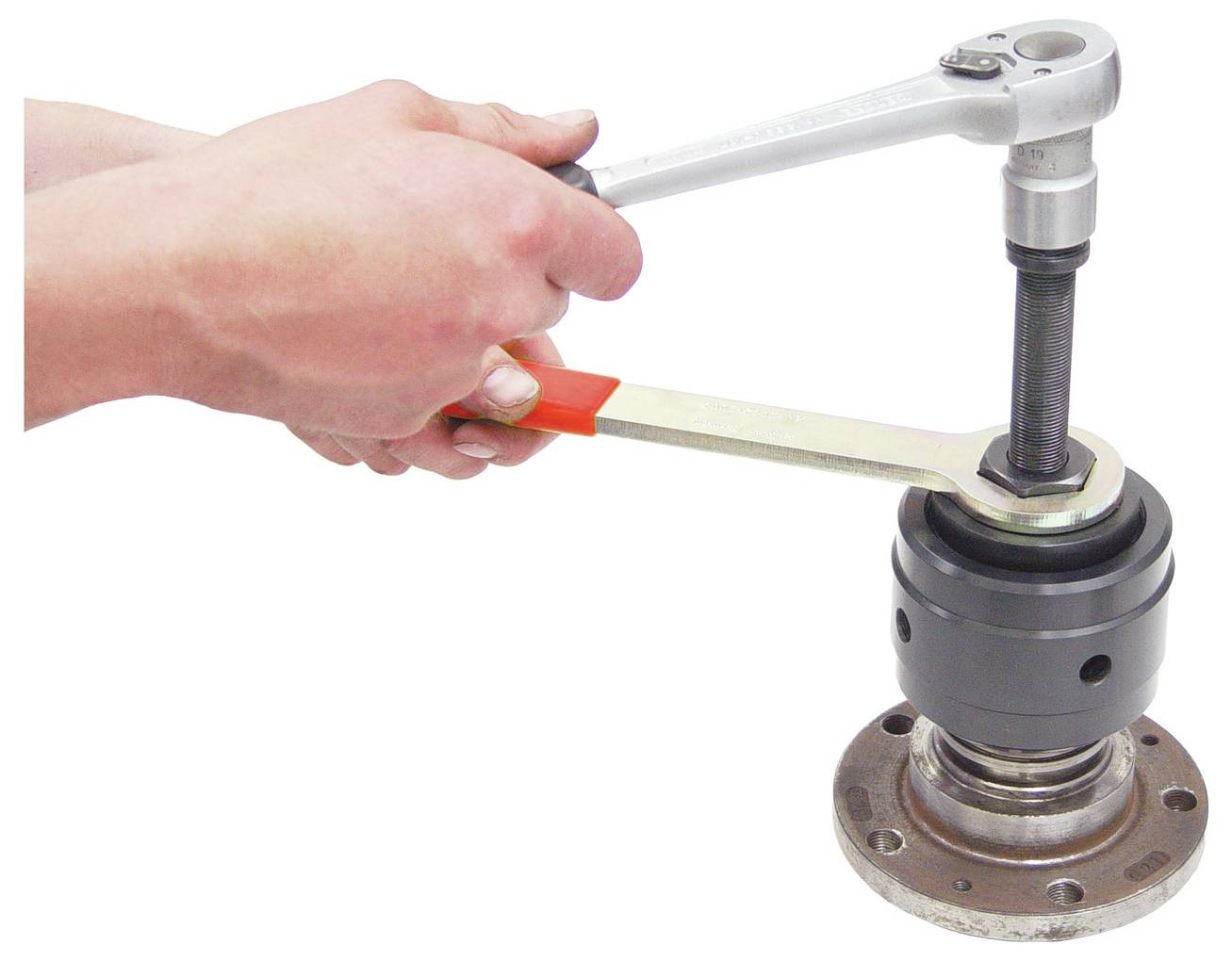 Una persona utilizza una chiave inglese e una chiave a tubo per stringere o allentare un componente meccanico, possibilmente un cuscinetto, su una base metallica.