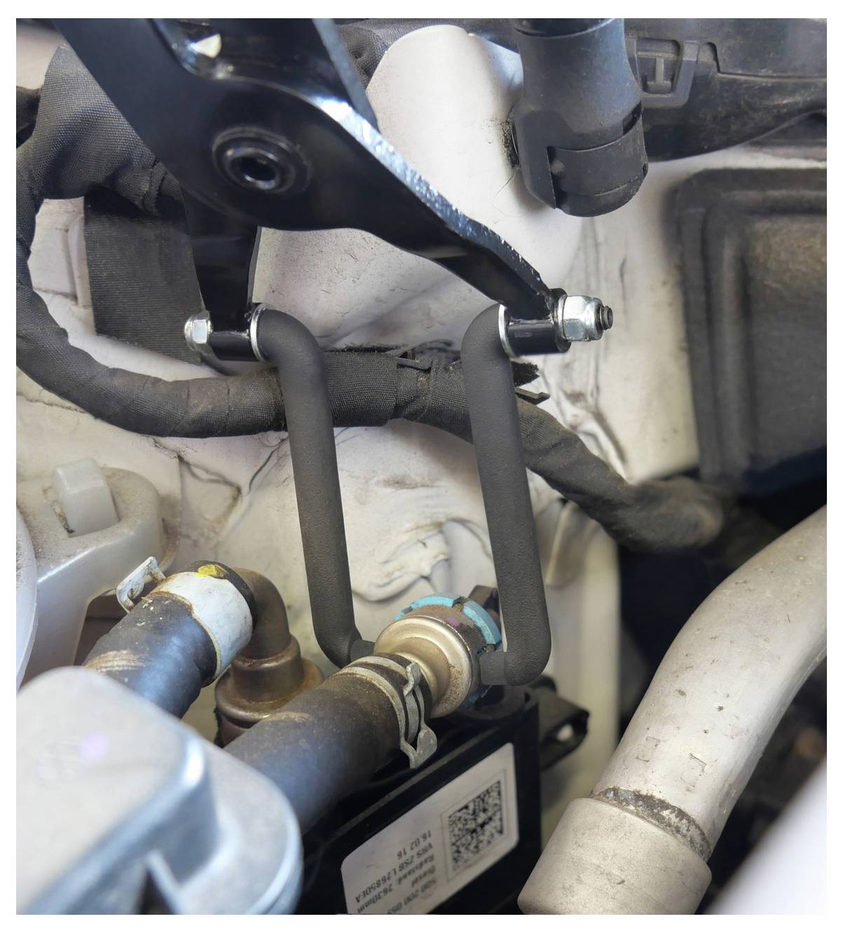 Un componente motore con una staffa metallica e tubi, collegato a un insieme meccanico più grande, che indica una parte di un sistema automobilistico.