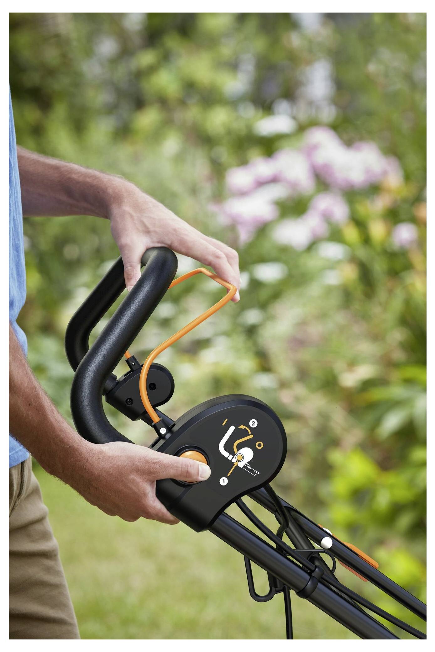 Una persona sta regolando il manico di uno strumento da giardinaggio con impugnatura ergonomica. Un giardino con fiori in fiore è visibile sullo sfondo.