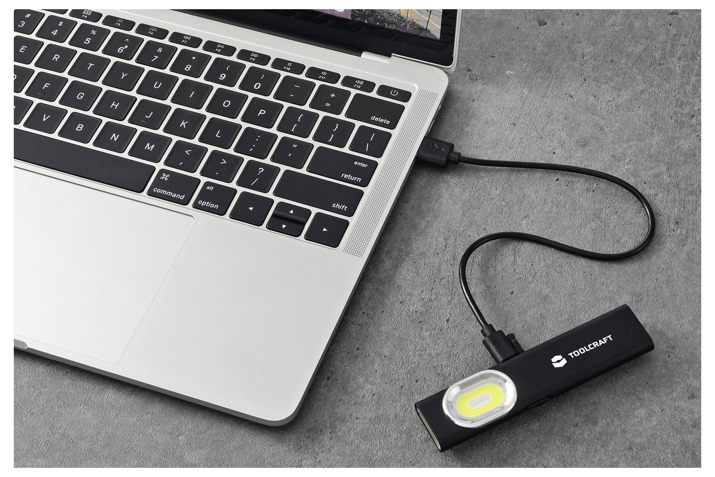Lampada da lavoro ricaricabile tramite USB collegata a un laptop via cavo, posizionata su un piano di lavoro grigio.