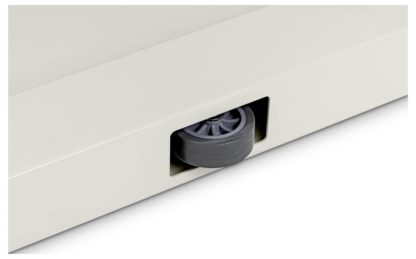 Un primo piano di una ruota grigia parzialmente incastrata in un angolo di una superficie piatta e chiara, probabilmente parte di un oggetto più grande o di un mobile.