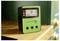 Un dispositivo verde mostra la concentrazione di radon su uno schermo. Si trova su uno scaffale di legno e ha tre pulsanti di controllo.