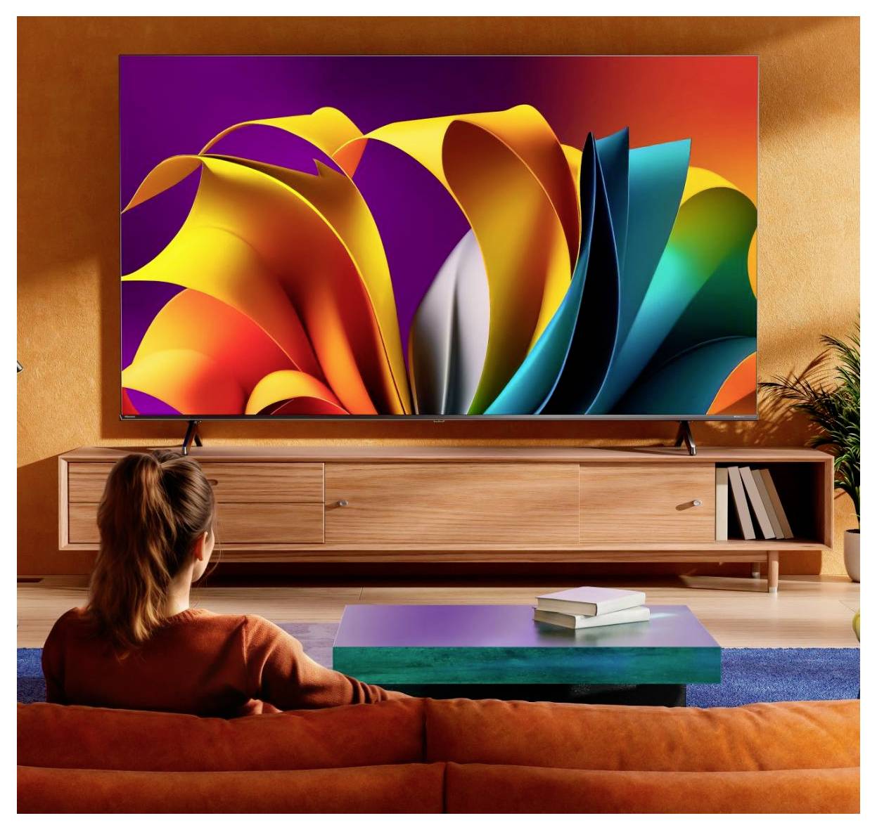 Una persona è seduta su un divano mentre guarda una grande televisione con forme astratte colorate e vivaci sullo schermo in un soggiorno illuminato calorosamente.