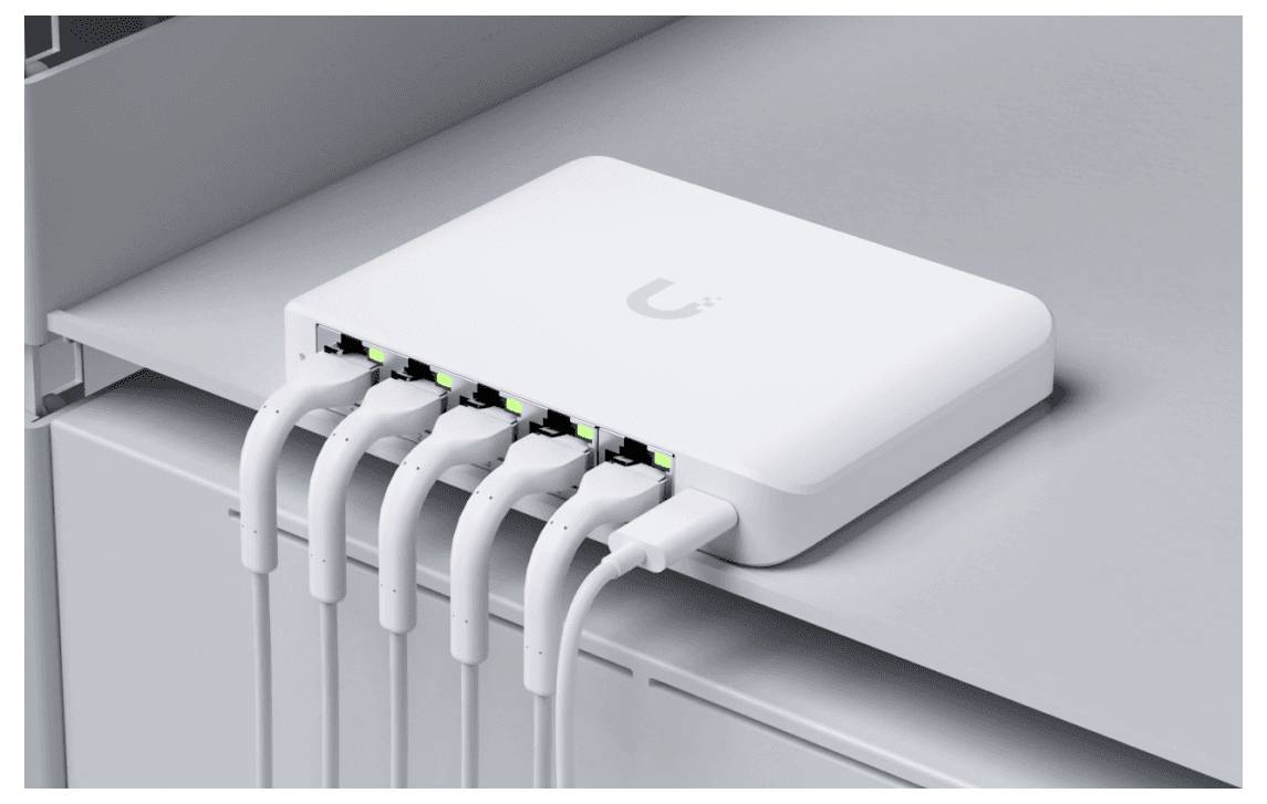 Un switch di rete bianco su uno scaffale collega più cavi Ethernet, indicati da spie di stato luminose, che suggeriscono connessioni attive.