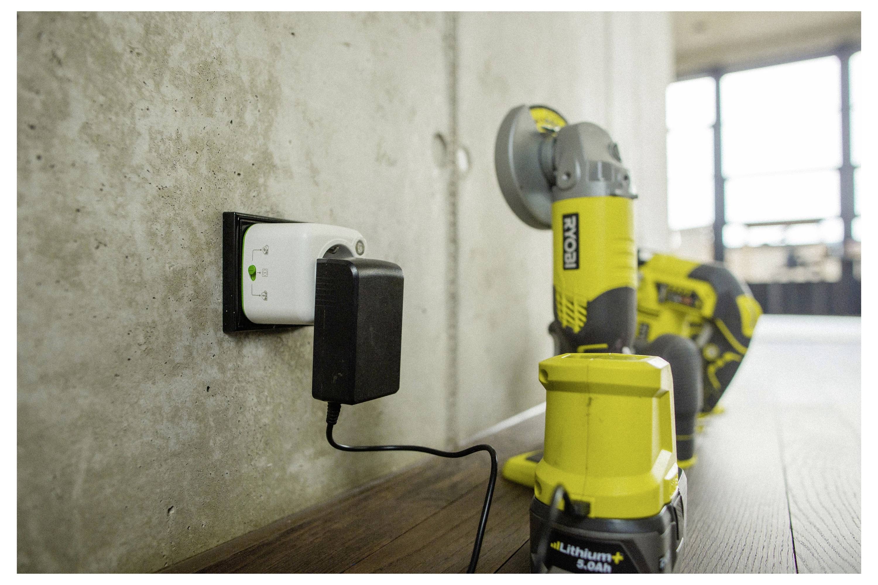 Un caricabatterie per utensili elettrici collegato a una presa con un trapano senza fili giallo e nero e una sega circolare su un pavimento in legno contro un muro in cemento.