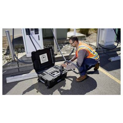Una persona che indossa un giubbotto di sicurezza sta utilizzando un dispositivo portatile presso una stazione di ricarica per veicoli elettrici. Il dispositivo è contenuto all'interno di una custodia nera.