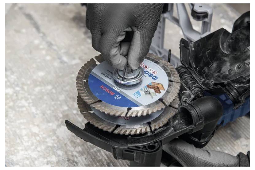 Le mani guantate installano una lama circolare Bosch su una sega elettrica con una chiave inglese.