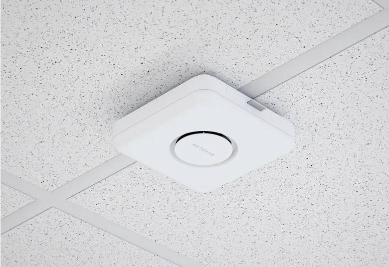 Un punto di accesso wireless quadrato bianco è montato su un soffitto punteggiato, posizionato centralmente all'interno di una griglia di piastrelle per soffitto.