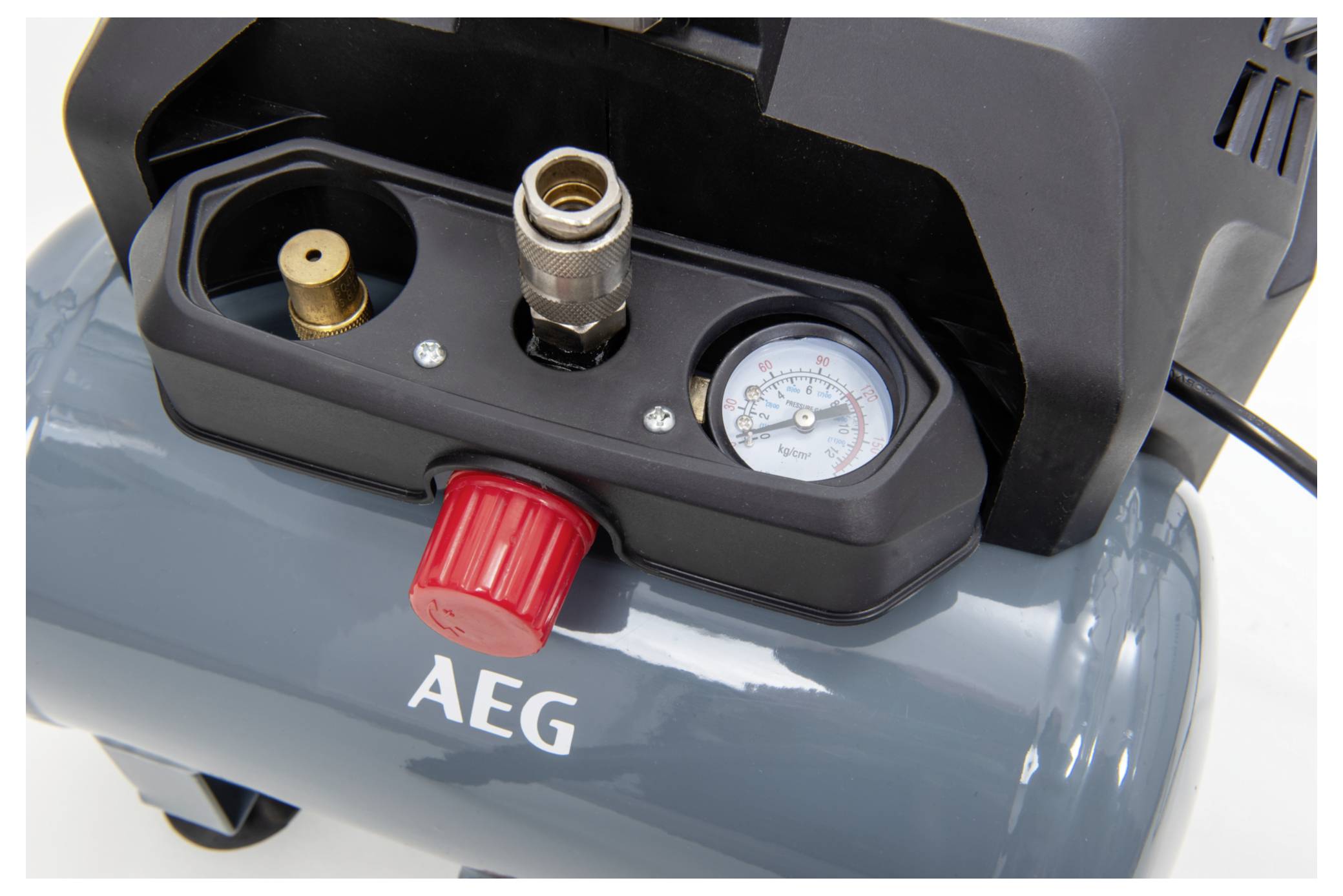 Una vista ravvicinata del compressore d'aria da un'angolazione superiore, che mostra un manometro, un raccordo in ottone e una manopola rossa su una base grigio scuro etichettata 'AEG'.
