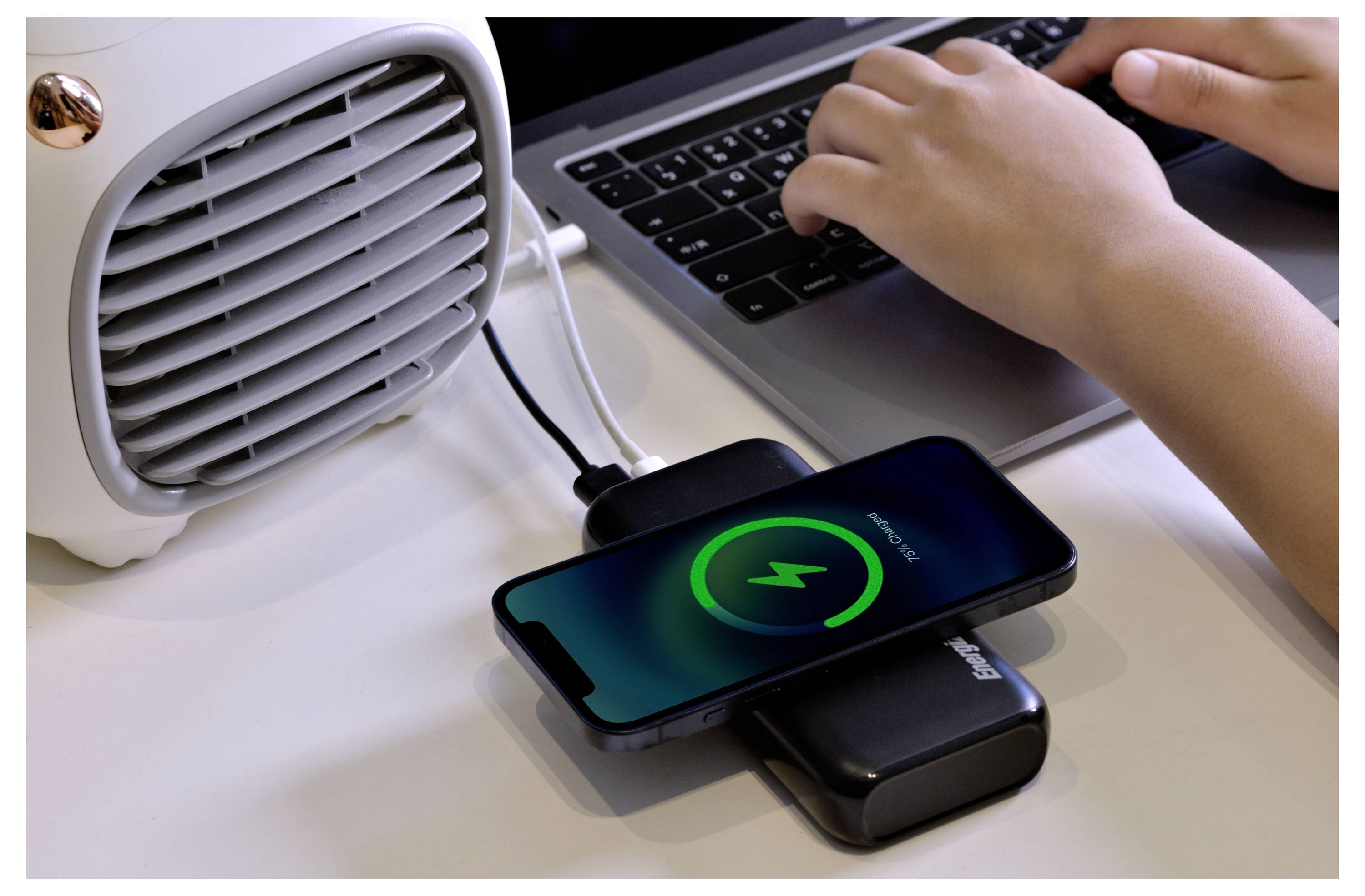Una persona digita su un laptop mentre uno smartphone si carica senza fili accanto a un piccolo riscaldatore su una scrivania.