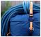 Uno zaino da arrampicata blu con una corda arrotolata collegata e cinghie arancioni. Lo sfondo è sfocato, suggerendo un ambiente esterno.