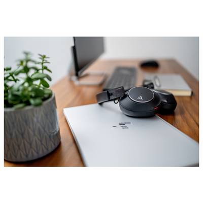 Uno spazio di lavoro elegante con un laptop, cuffie wireless, una piccola pianta, un monitor da desktop, una tastiera e un quaderno chiuso su una scrivania in legno.