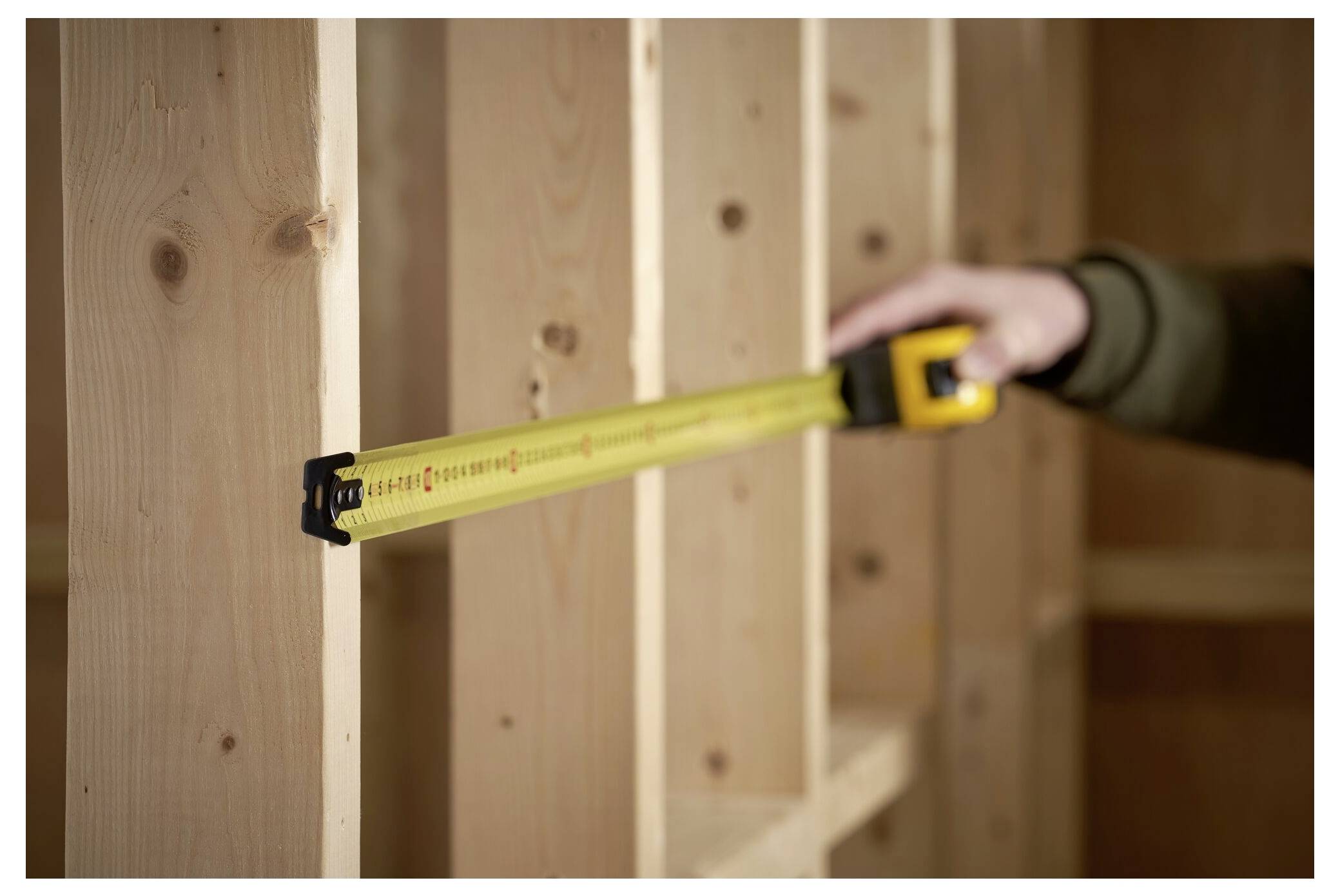 Una persona misura travi di legno con un metro a nastro giallo, allineandolo tra i supporti verticali, il che suggerisce lavori di costruzione o carpenteria.
