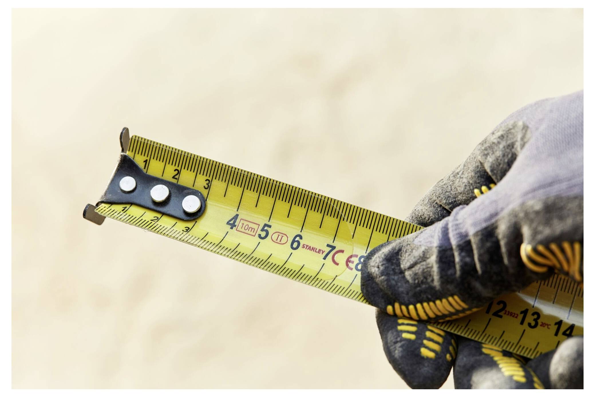 Una persona utilizza un soffiatore manuale giallo per eliminare la polvere dal pavimento di un cantiere edile, circondato da telai in legno e muri in compensato.
