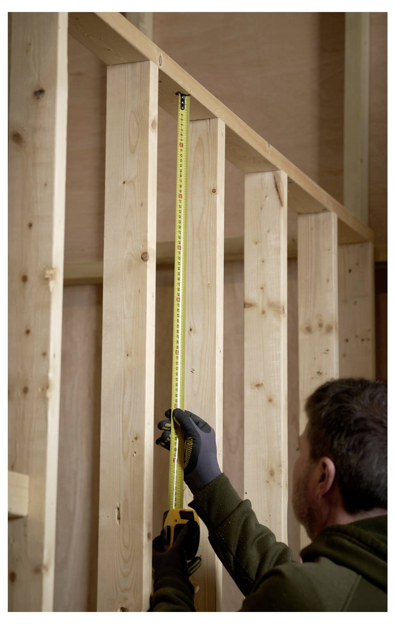 Una persona che indossa guanti utilizza un metro a nastro su una struttura in legno, probabilmente mentre lavora su un progetto di costruzione o carpenteria all'interno di un edificio.