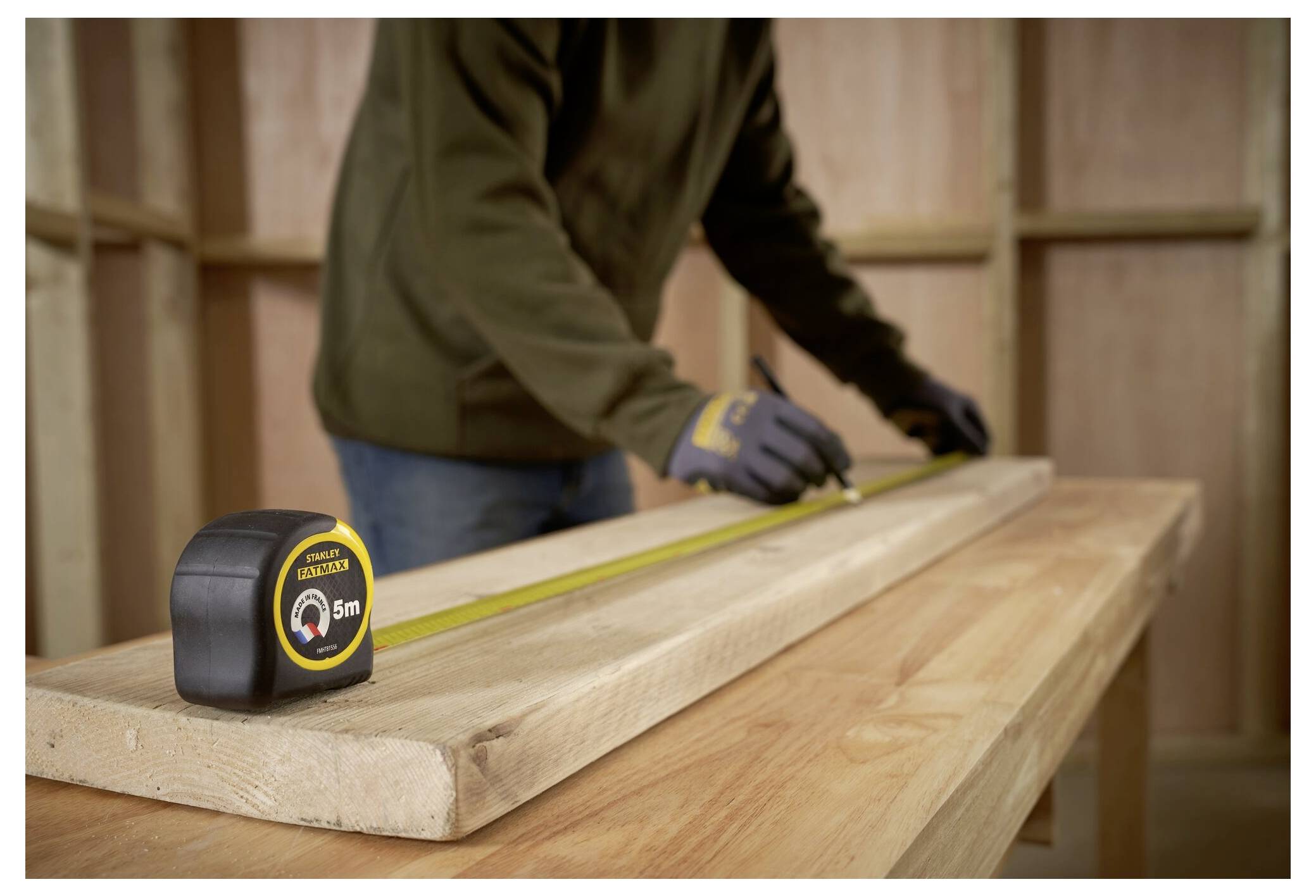 Una persona misura una tavola di legno con un metro a nastro su un banco da lavoro, indicando un'attività di carpenteria o costruzione.